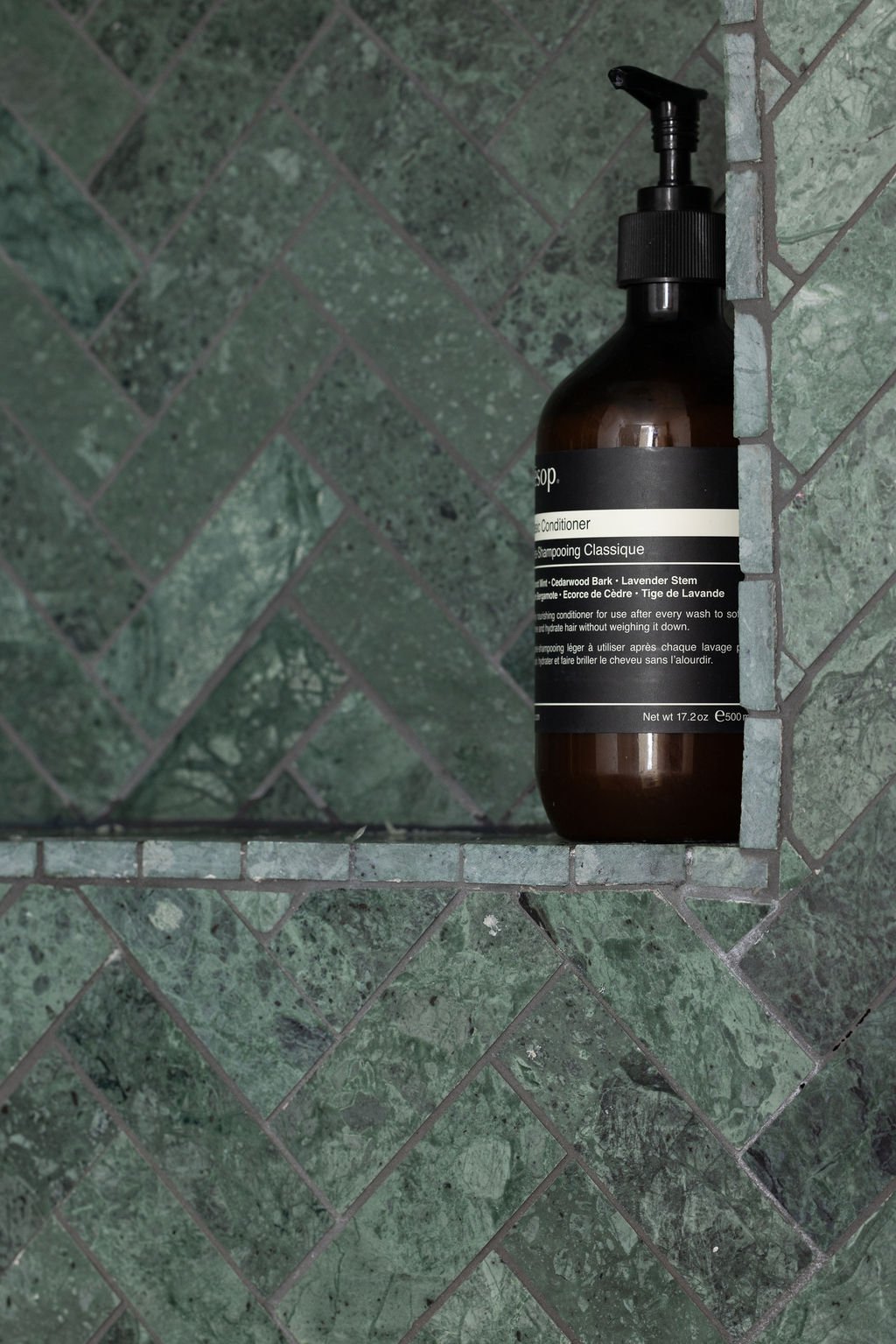 Close-up of textured deep green stone tile arranged in a herringbone pattern inside the bathroom shower.