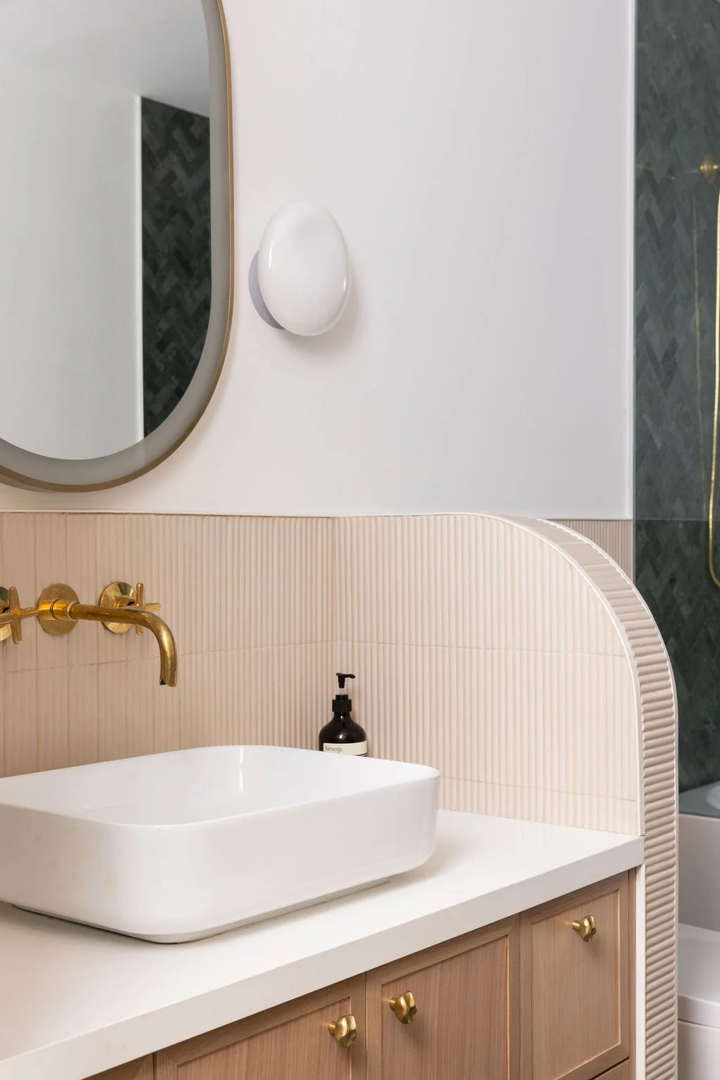 Primary bathroom at Ritchie Residence in Toronto, designed by Flodström Interiors, featuring pale pink fluted wall tiles, a brass faucet, white sink and rounded mirror.