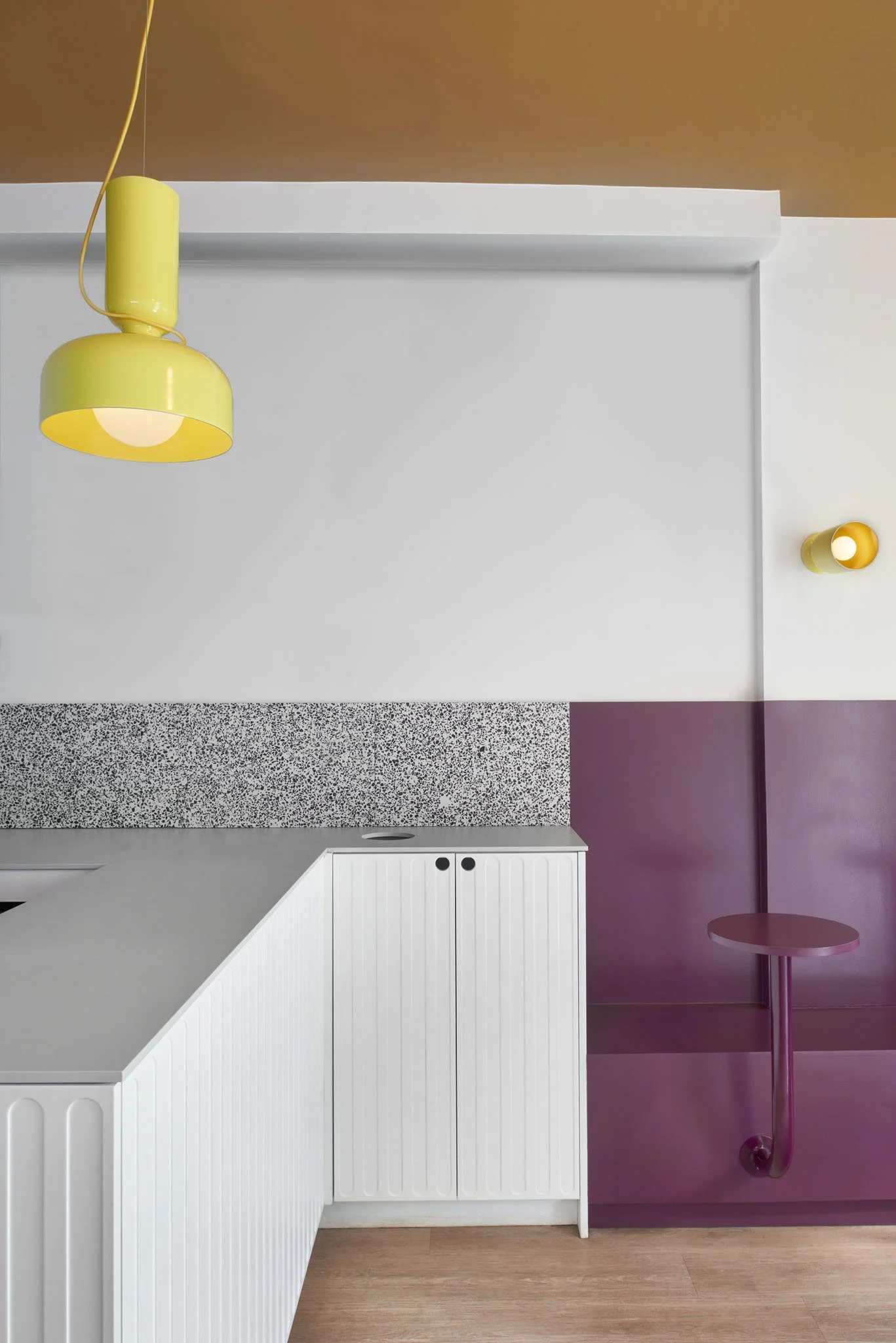 Fantasy Kitchen restaurant interior with white fluted counter, speckled backsplash, purple wall panelling and yellow pendant lighting.