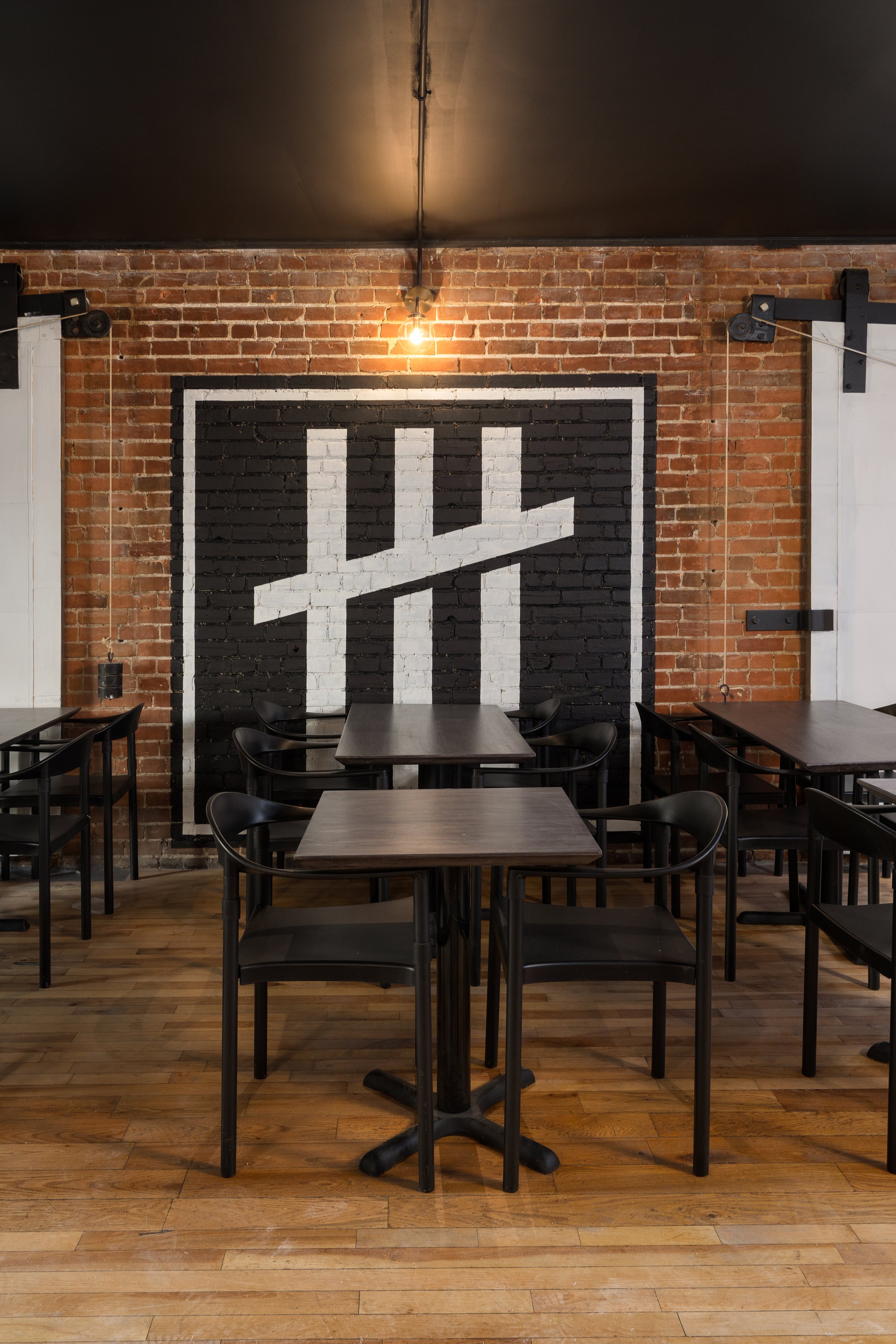 Dining area at Turbo Haüs with black furniture, exposed brick and a large black-and-white graphic painted on the wall.