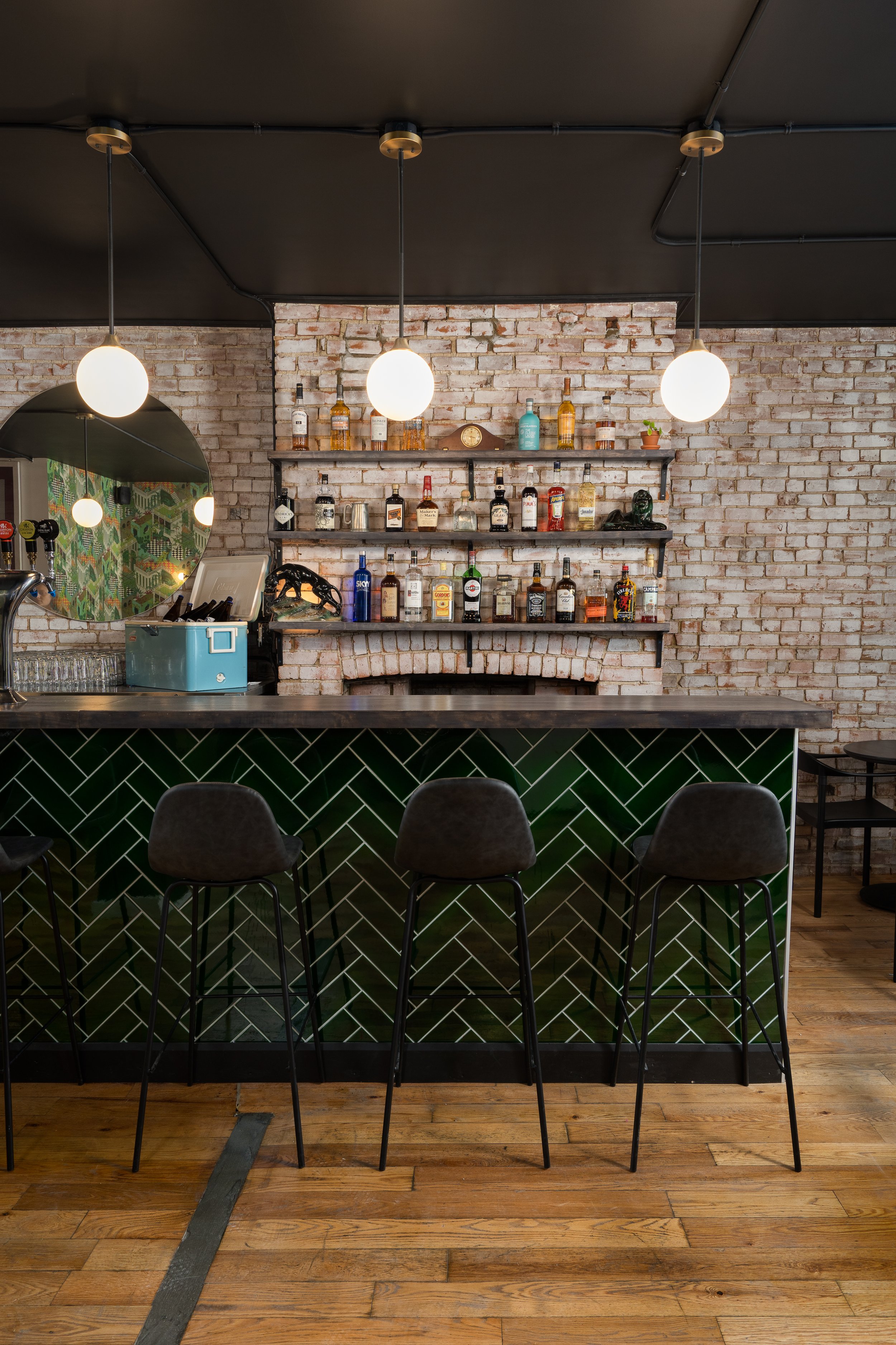 Wide view of the Turbo Haüs bar with green tiled frontage, black bar stools, exposed brick walls and globe pendant lighting.
