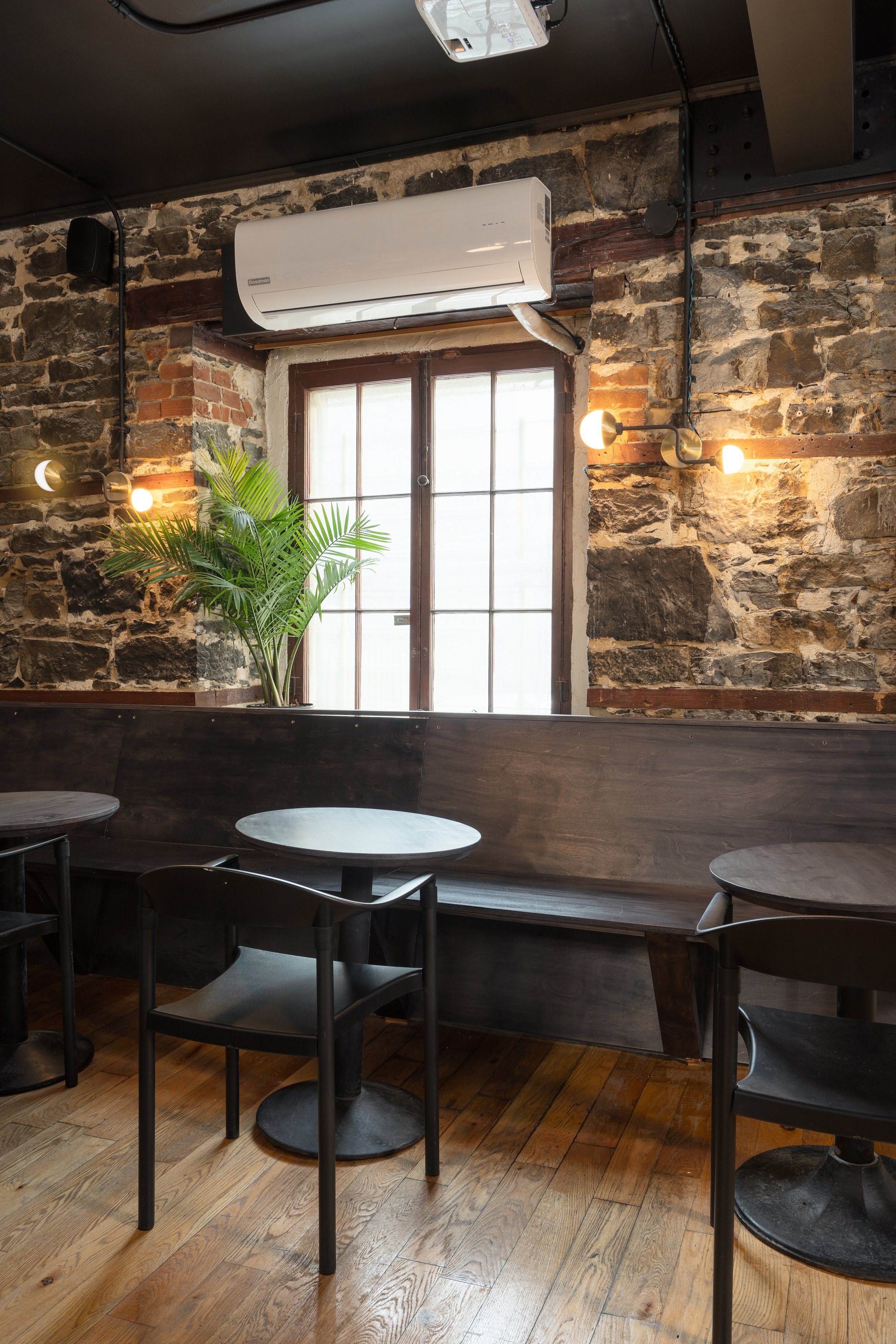 Dark timber banquette seating with small round tables, black chairs and exposed stone walls in the Montréal music venue.