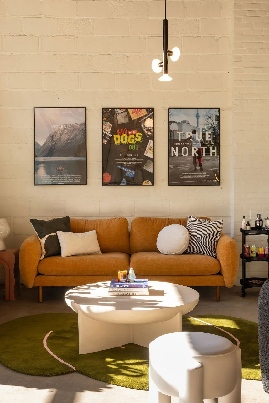 Contemporary office lounge with a rust-coloured sofa, sculptural white coffee table, olive green rug and framed artwork at Farmhouse Creative Labs.