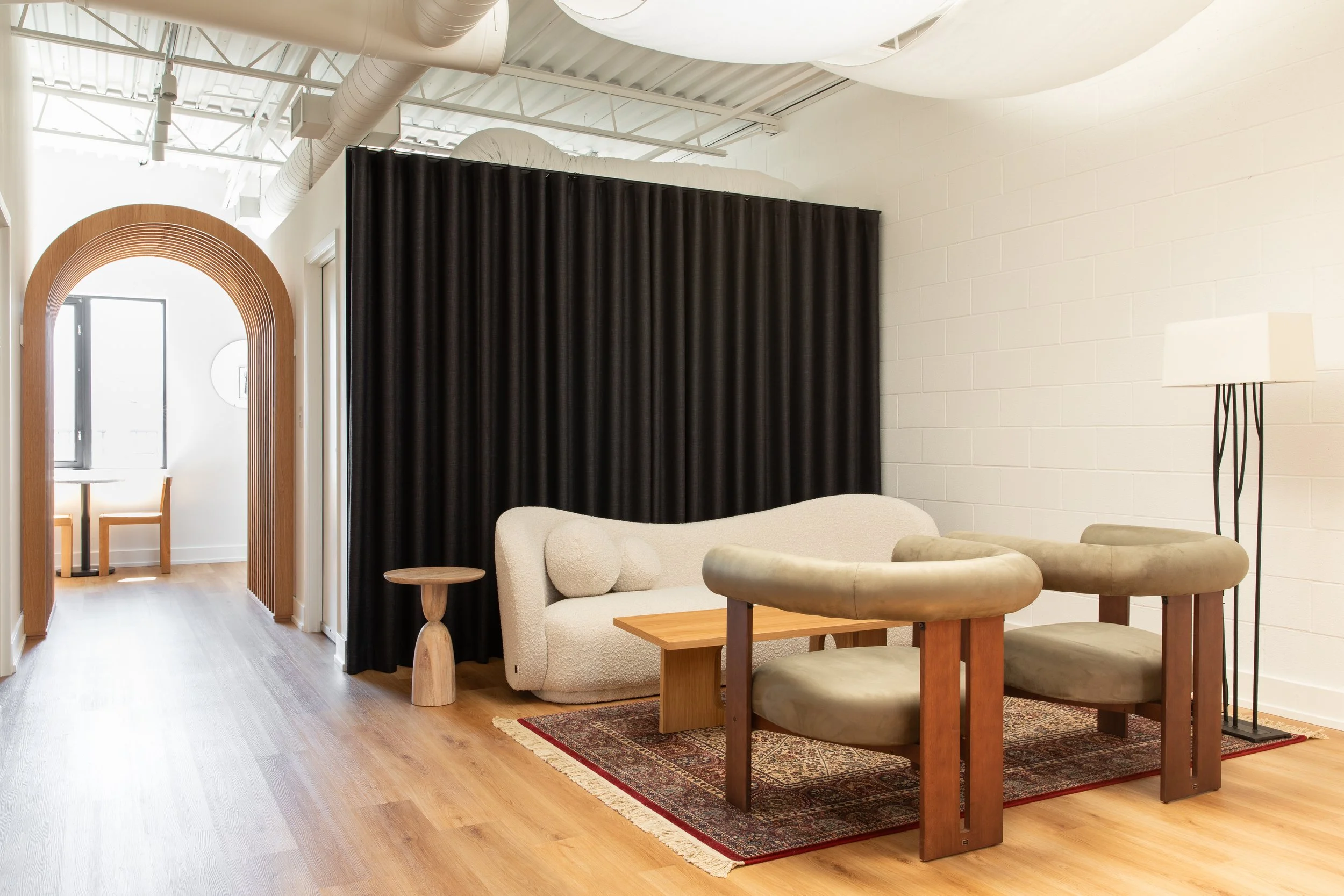 Creative studio lounge at Wonderlit Studios in Toronto, designed by Flodström Interiors, featuring a curved wood archway, cream sofa, sculptural seating and black curtain partition.
