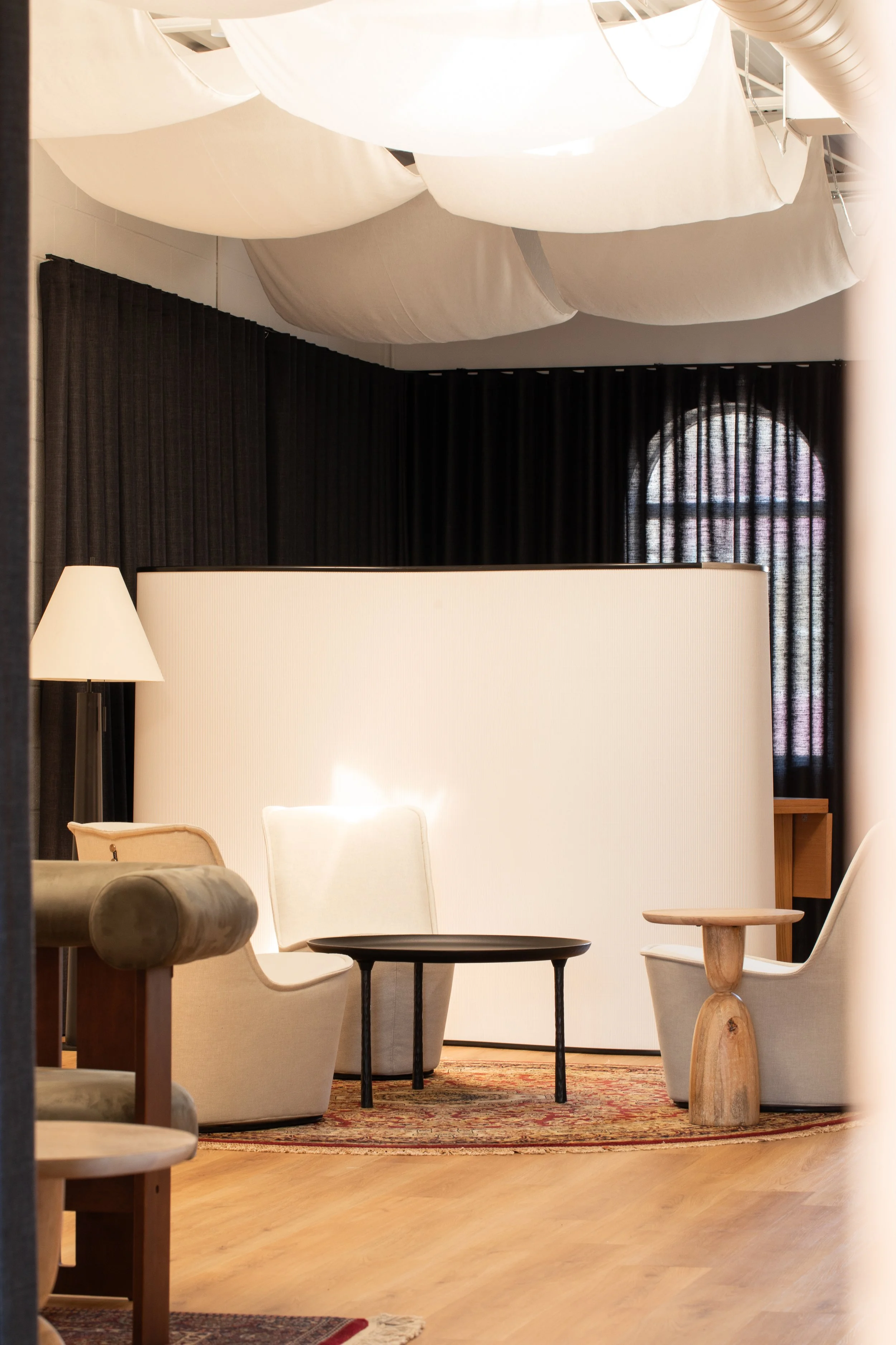 Wonderlit Studios lounge with cream chairs, black curtains, a patterned rug and softly draped white ceiling fabric.