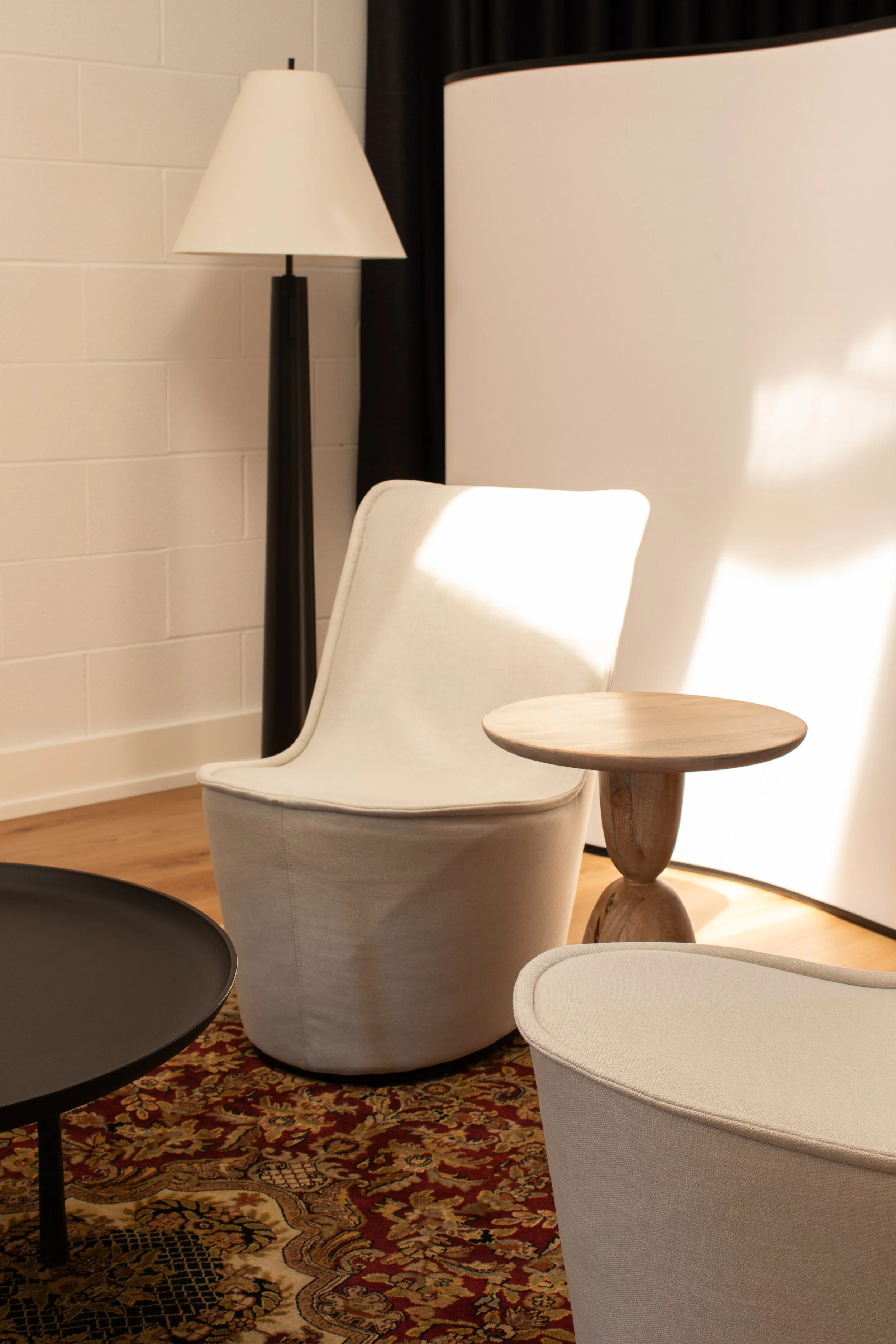 Cream upholstered lounge chairs, a sculptural wood side table and a floor lamp in a softly lit studio seating area.