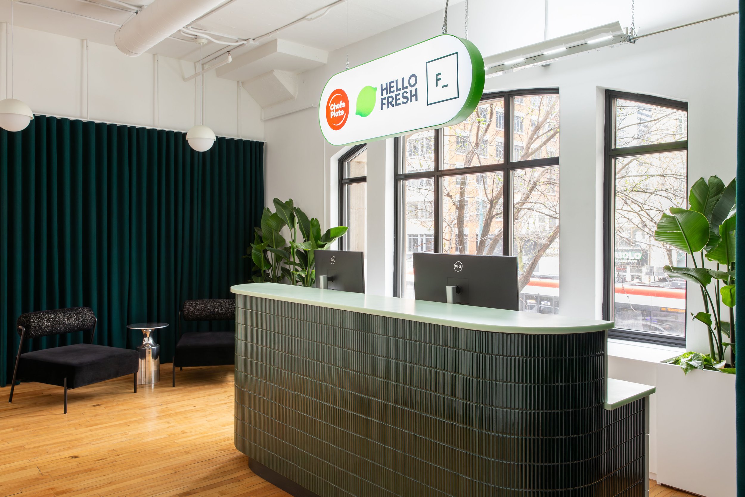 Reception area at the HelloFresh, Chef's Plate and Factor Toronto offices, designed by Flodström Interiors, featuring a dark green tiled reception desk, curved signage and large industrial windows.