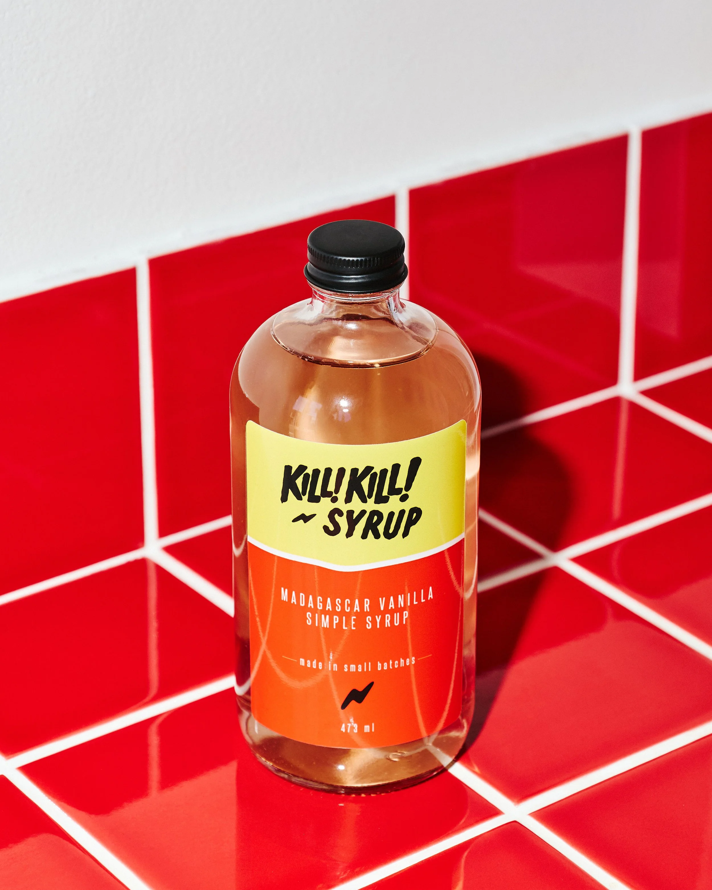 Kill! Kill! Coffee Madagascar vanilla simple syrup bottle with a custom yellow and red label, photographed against red café tiles.