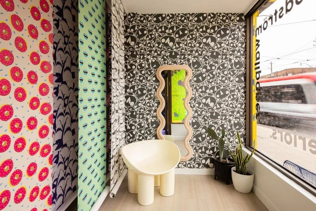 Flodström wallpaper display featuring colourful patterns beside a sculptural cream chair and wavy mirror in a Toronto studio.