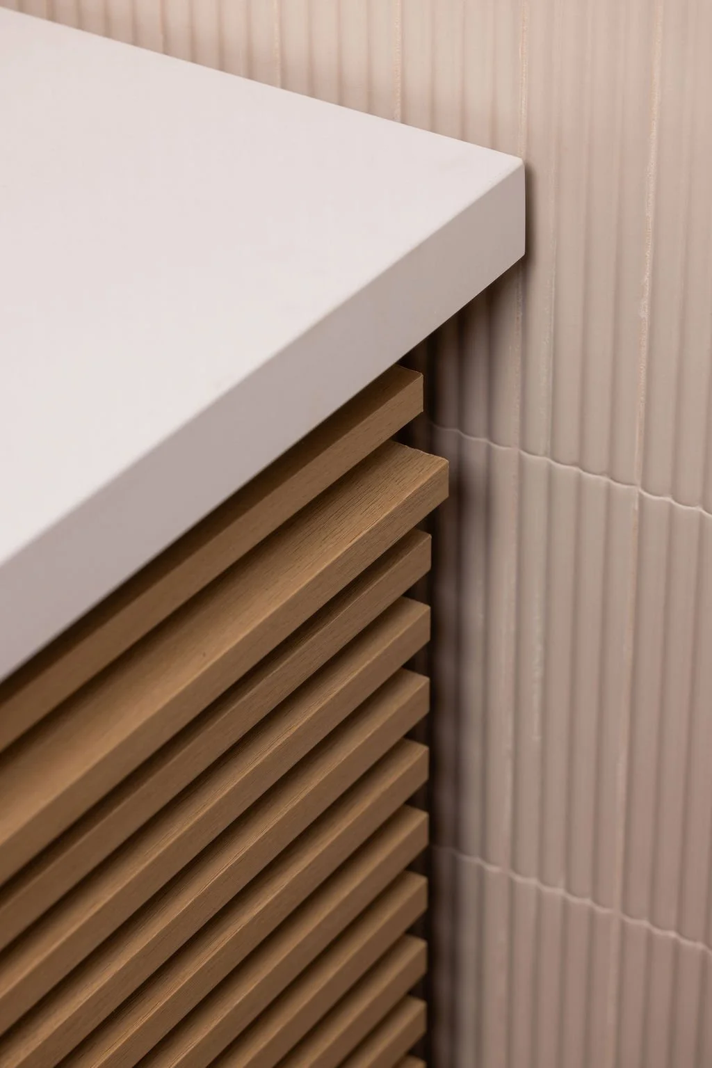 Close-up of horizontal wood slats on the custom powder room vanity beside pale vertically fluted wall tile.
