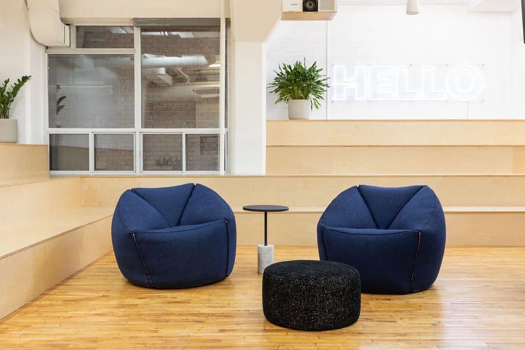 Contemporary lounge at the HelloFresh, Chef's Plate and Factor Toronto offices, designed by Flodström Interiors with sculptural blue chairs, a black ottoman and tiered pale wood seating.