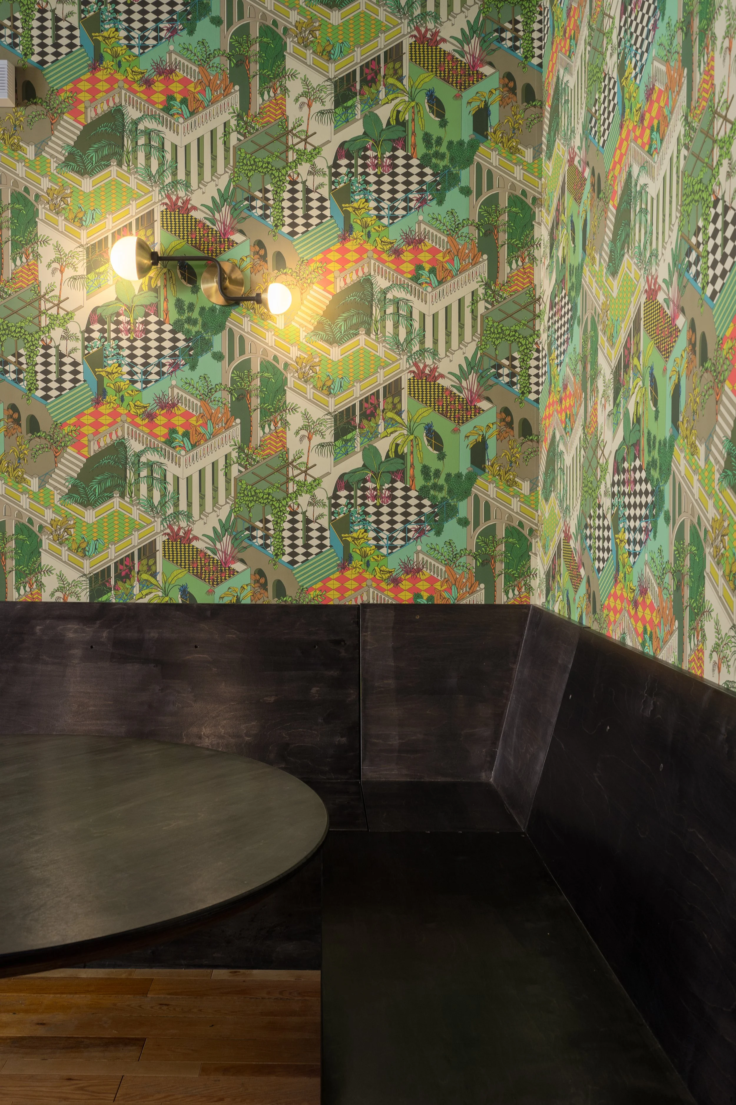 Colourful architectural and botanical wallpaper above dark wood banquette seating in the Montréal bar.