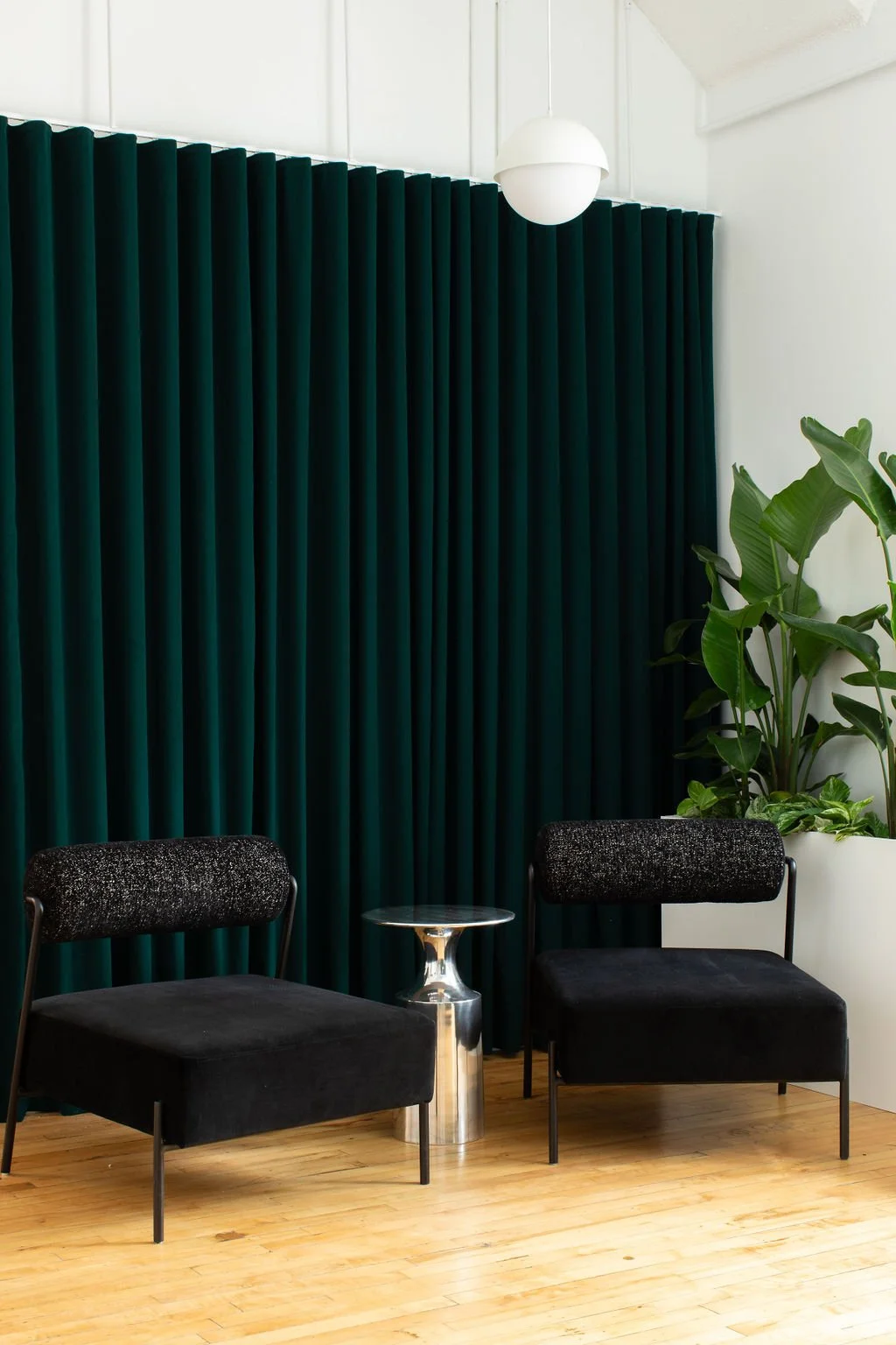 Reception waiting area at the HelloFresh, Chef's Plate and Factor Toronto offices, designed by Flodström Interiors with black upholstered lounge chairs, a silver side table and dark green curtains.