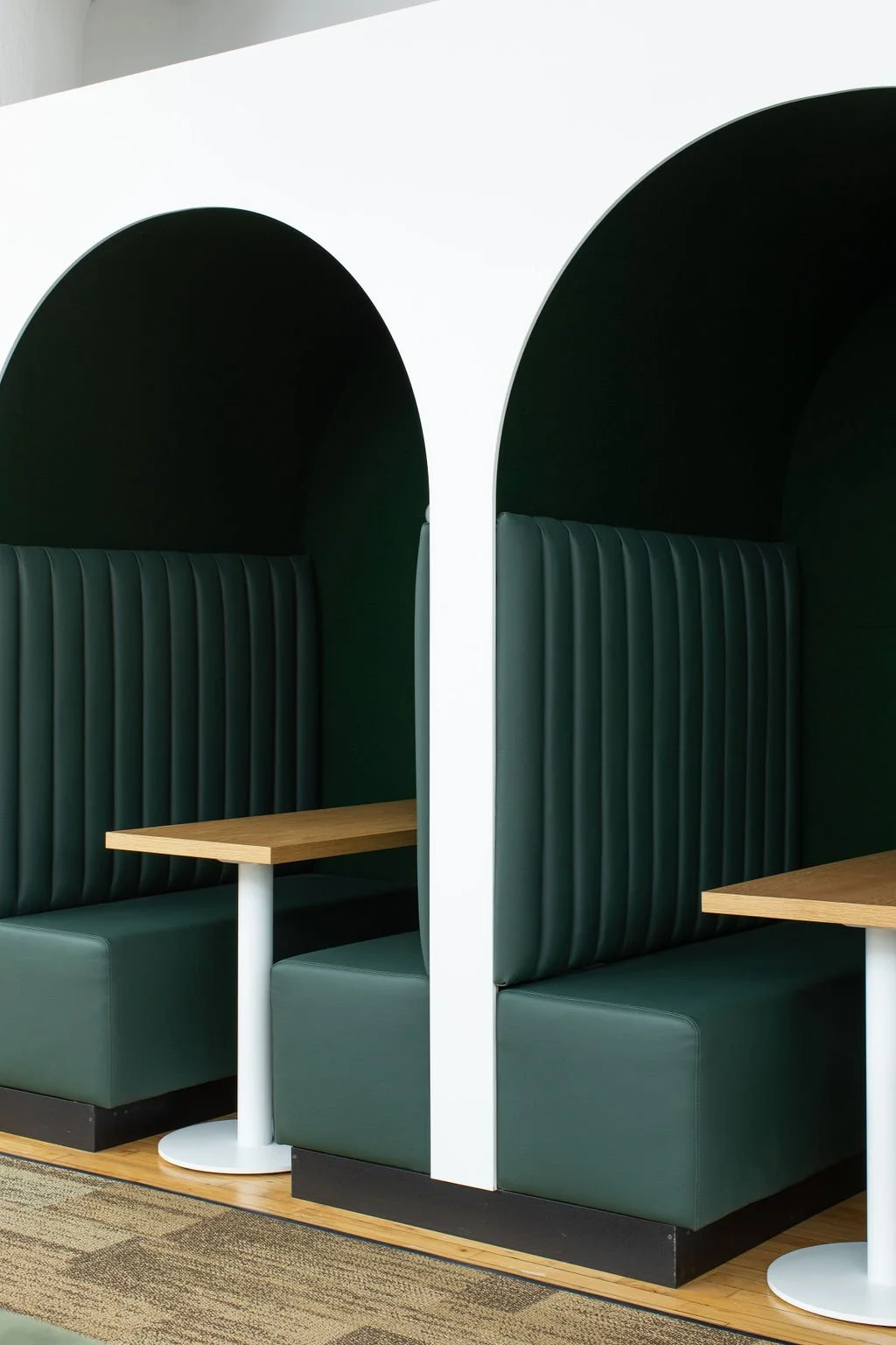 Built-in meeting booths at the HelloFresh Toronto office designed by Flodström Interiors, featuring deep green upholstered banquettes, arched partitions and light wood tables.