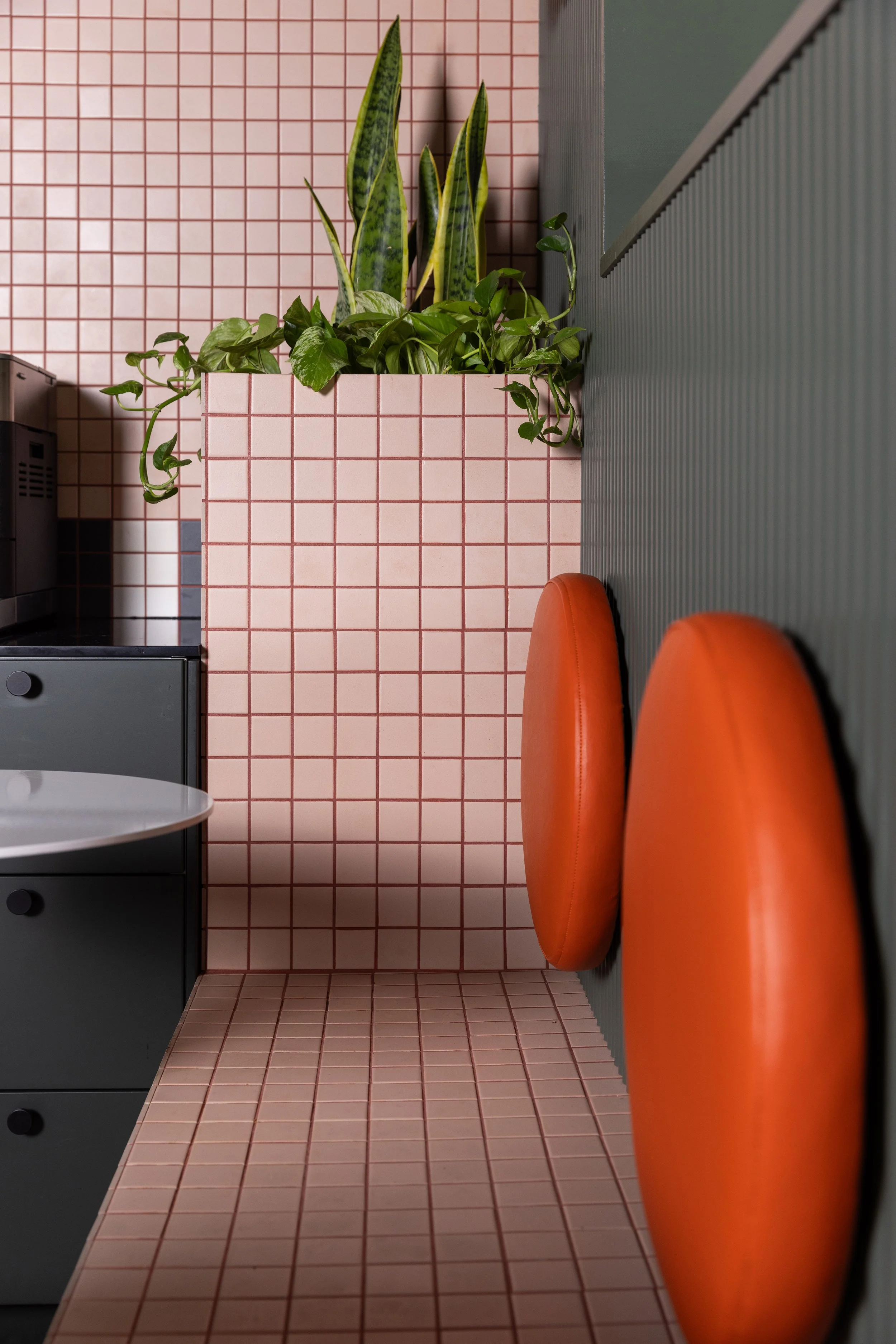 Close-up of custom pink tiled bench seating with bright orange circular backrests and a built-in planter at Farmhouse Creative Labs.
