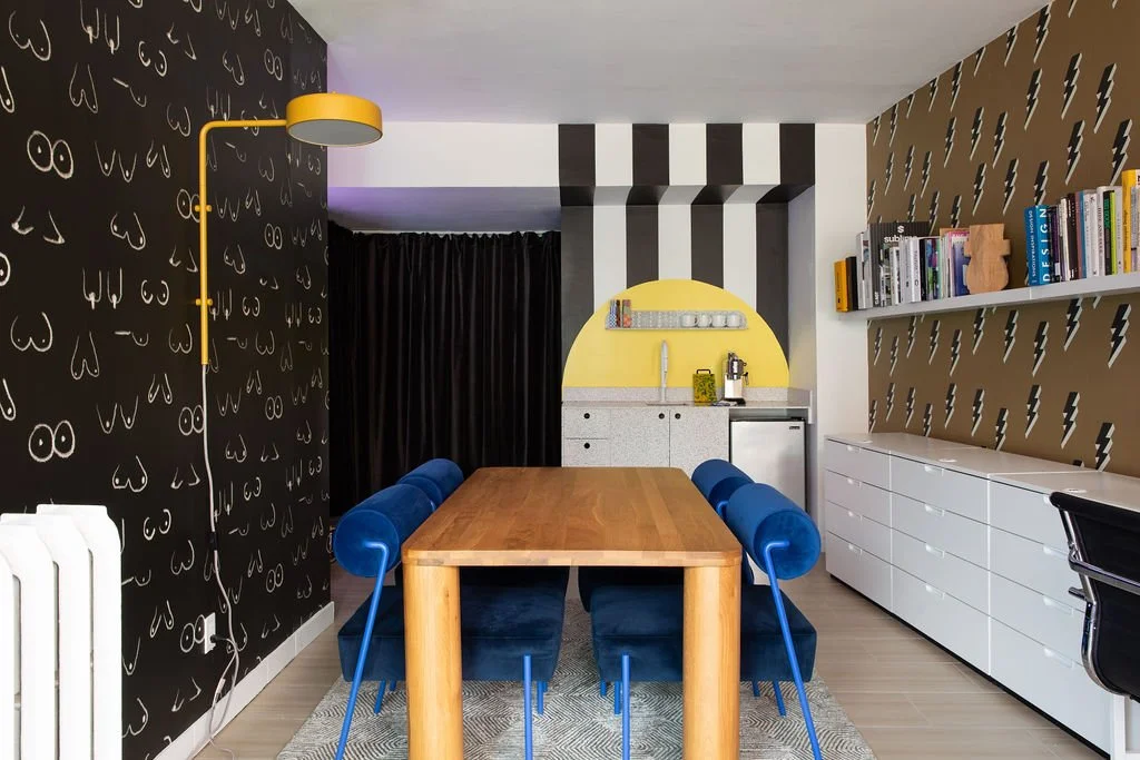 Flodström's Toronto creative design studio featuring a wood meeting table, cobalt blue seating, graphic wallpaper and a yellow wall lamp.