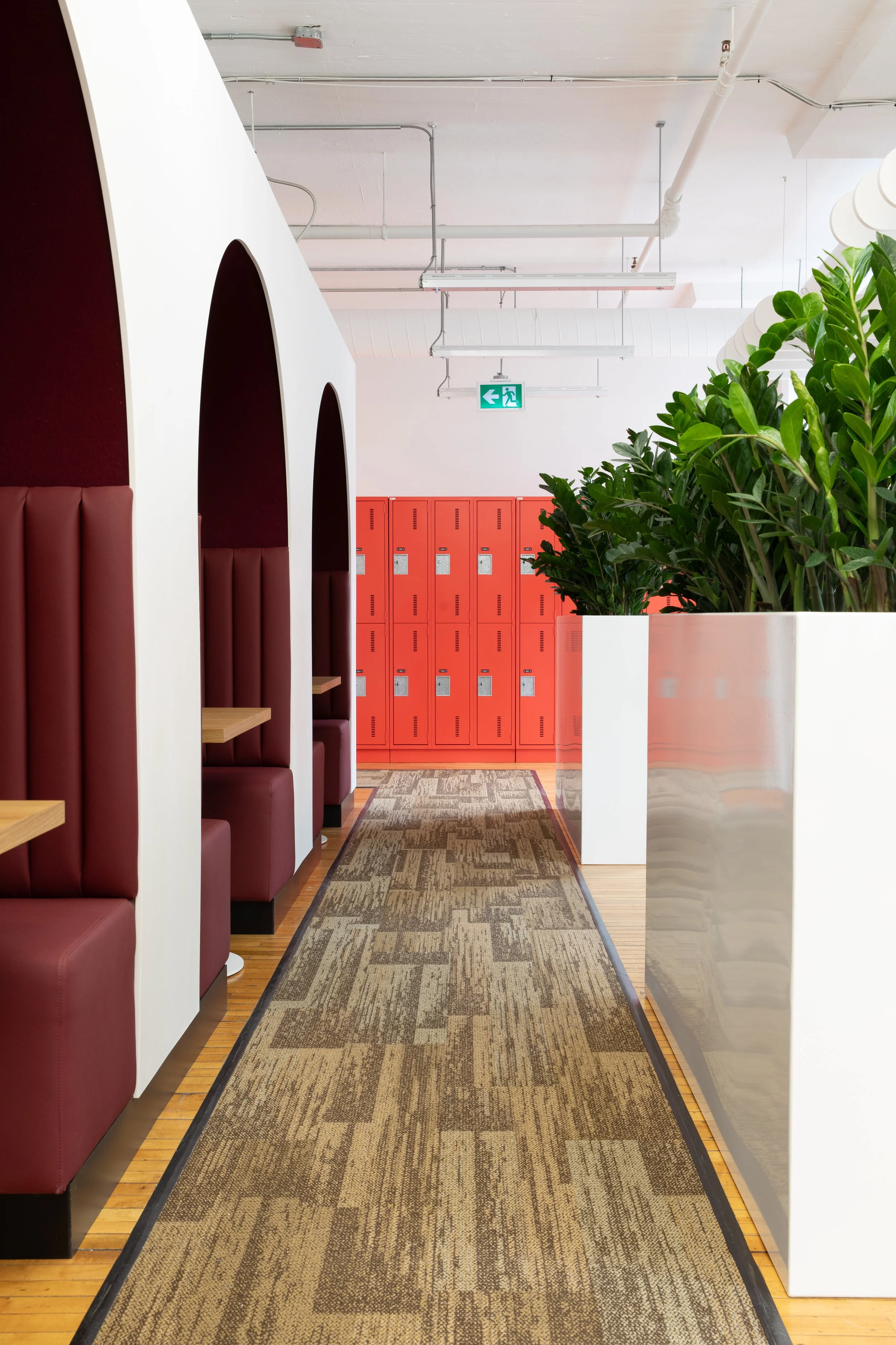 Toronto office interior for HelloFresh and Chef’s Plate, designed by Flodström Interiors, featuring red lockers, burgundy arched seating booths and greenery.