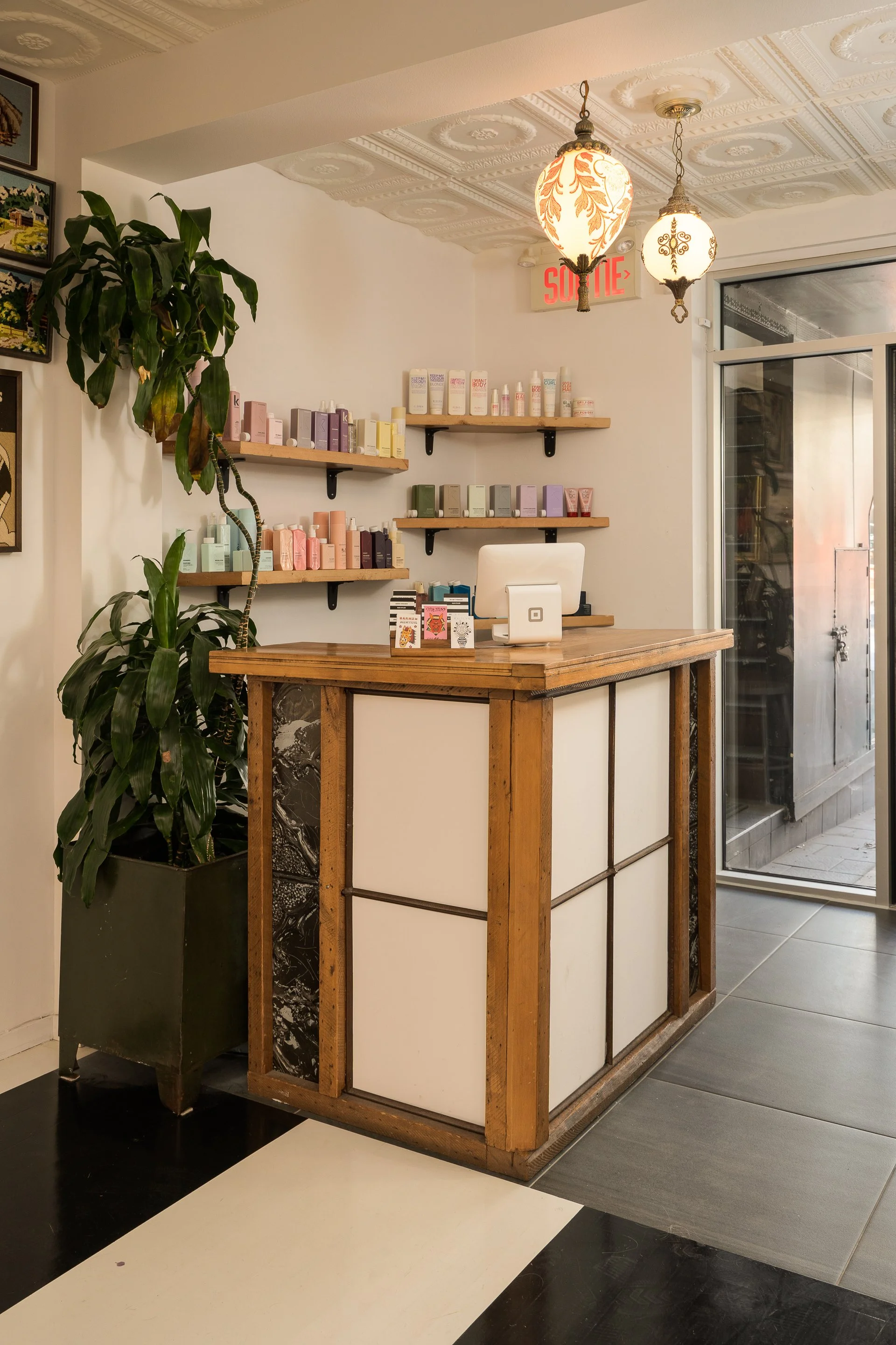 Two Horses reception counter with rustic wood framing, product display shelves, hanging pendant lights and indoor plants.