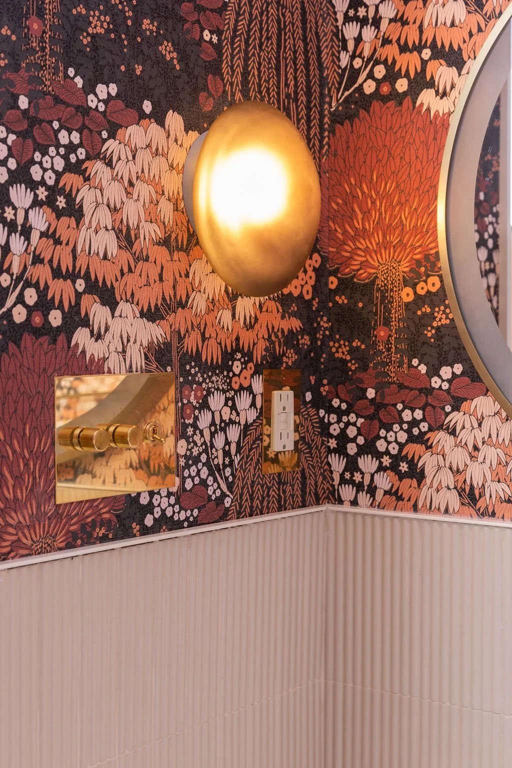 Brass wall sconce and decorative hardware against richly patterned floral wallpaper in the Ritchie Residence powder room.
