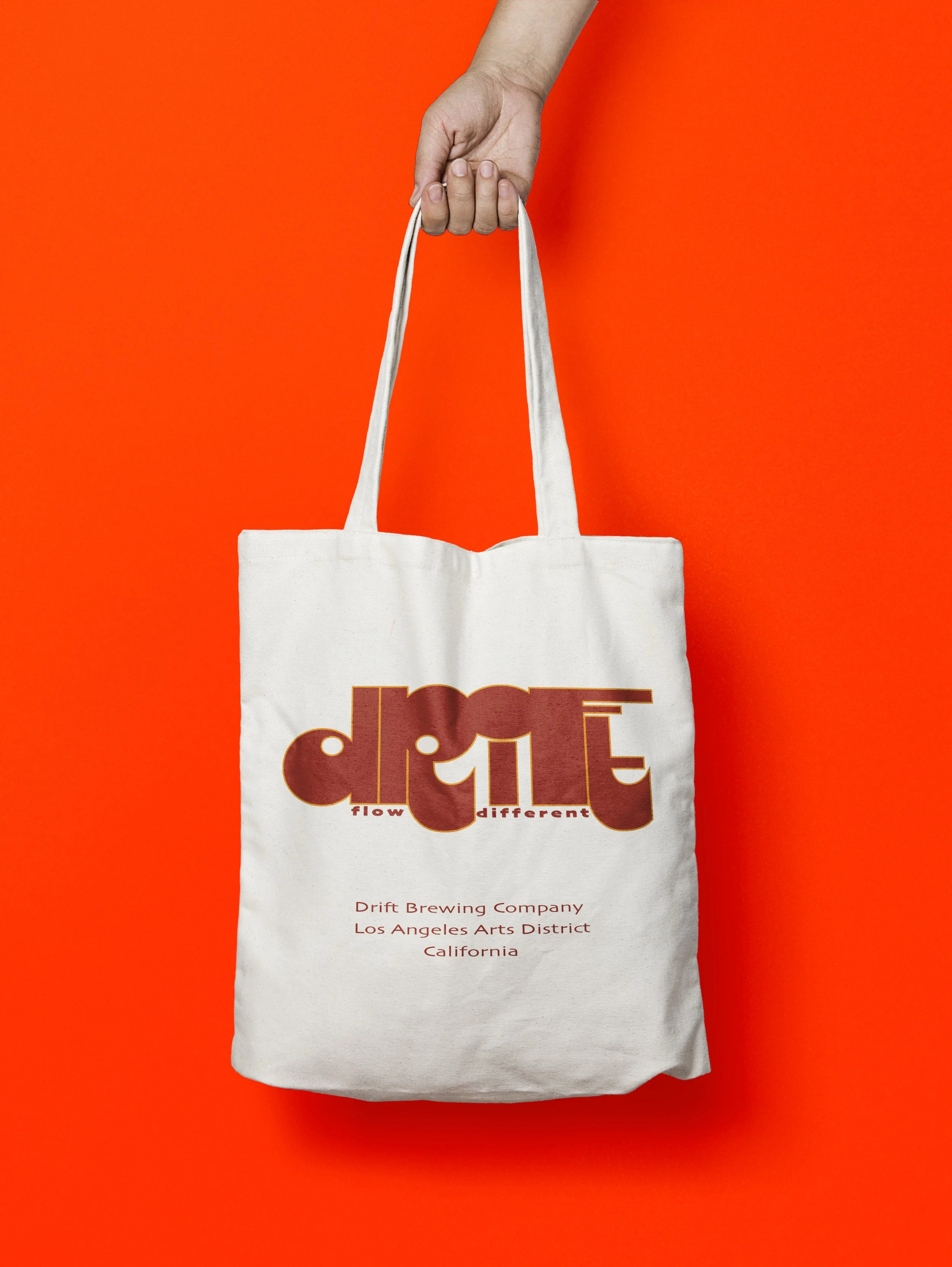 Cream canvas tote bag mockup featuring the Drift Brewery logo in burgundy and gold with the Flow Different tagline.