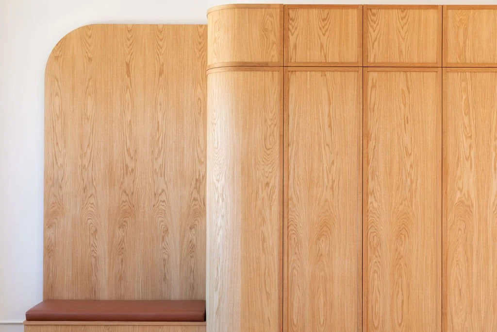 Custom oak cabinetry designed by Flodström Interiors, featuring curved corners, vertically grained wood panels and an integrated bench with a terracotta upholstered cushion.