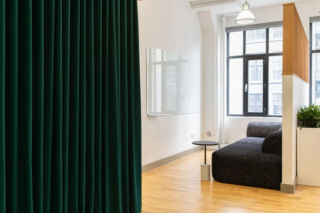 Private lounge area in the HelloFresh, Chef's Plate and Factor Toronto offices, designed by Flodström Interiors with dark green curtains, a charcoal upholstered sofa and natural light from industrial windows.