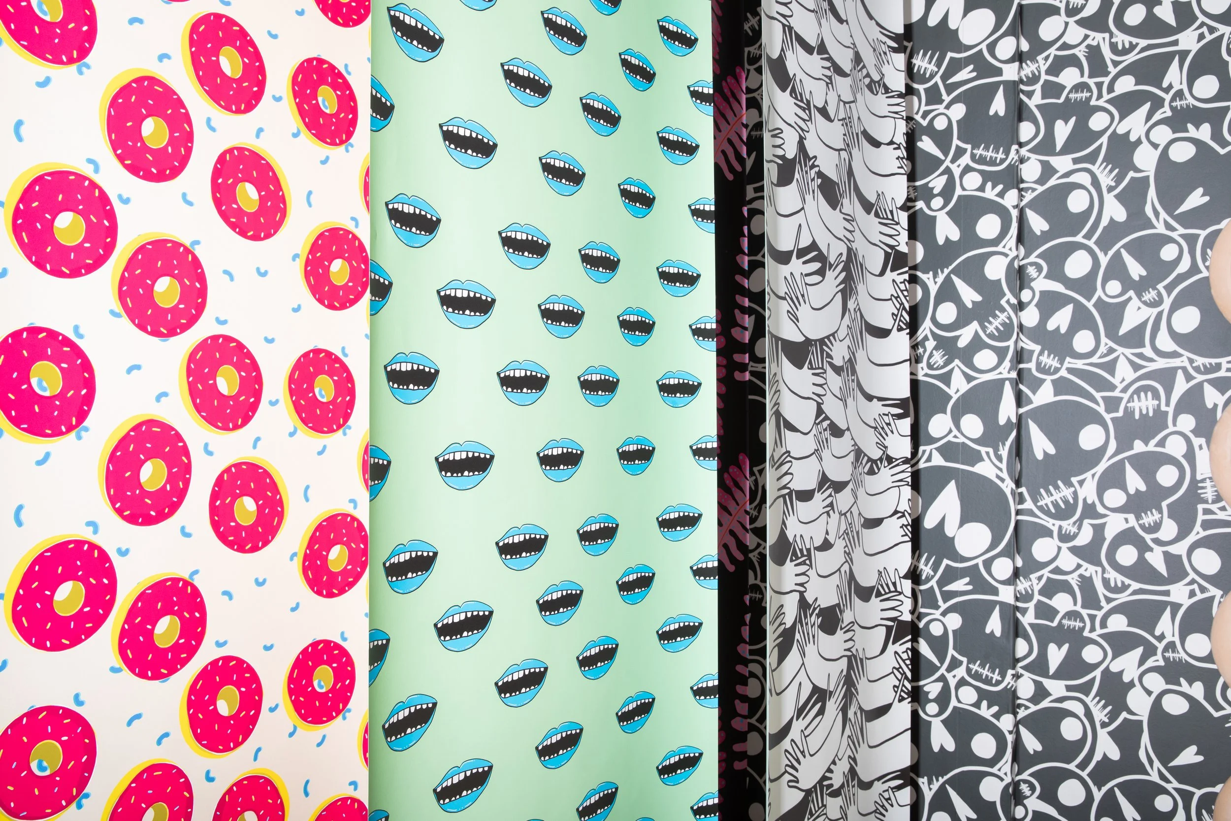 Colourful flodström wallpaper designs displayed in hanging panels, featuring pink doughnuts, blue mouths and black-and-white illustrations.