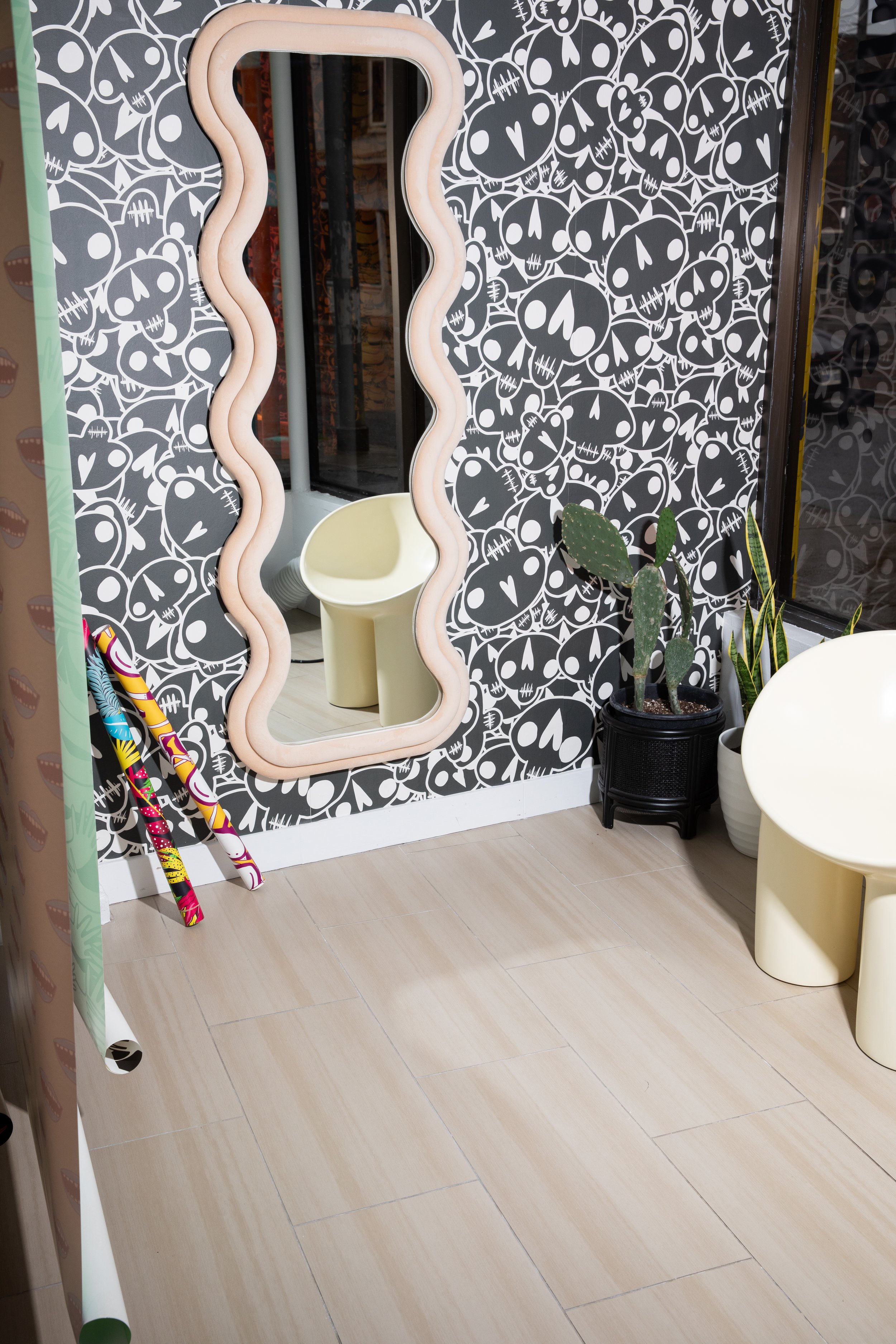 Black-and-white graphic wallpaper displayed behind a wavy cream mirror, sculptural chair and potted plants.
