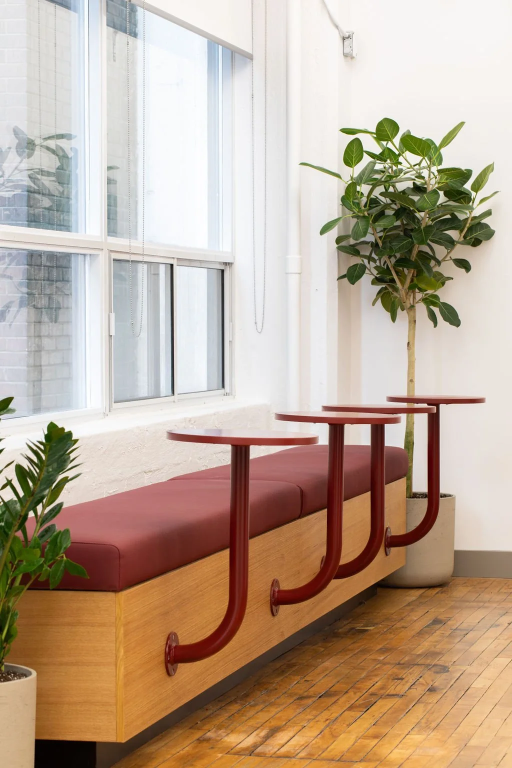 Custom banquette seating at the Chef's Plate Toronto office, designed by Flodström Interiors, featuring a long burgundy upholstered bench, red metal tables and indoor greenery.