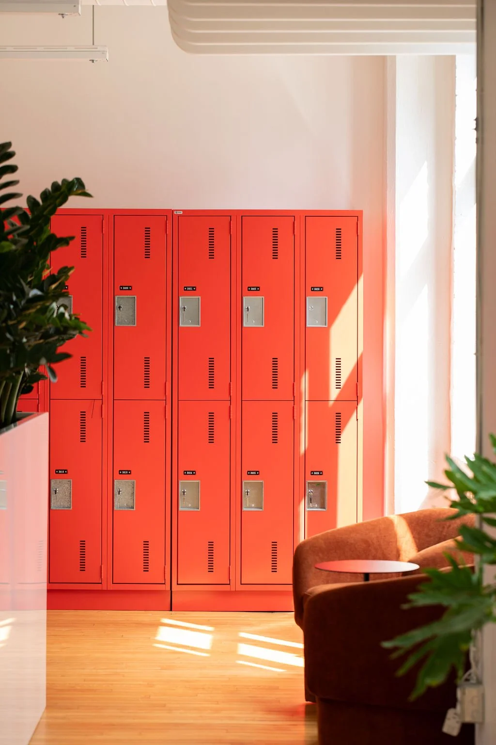 Bright red employee lockers at the Chef's Plate Toronto office, designed by Flodström Interiors, with warm wood flooring, a rust-coloured lounge chair and natural light.