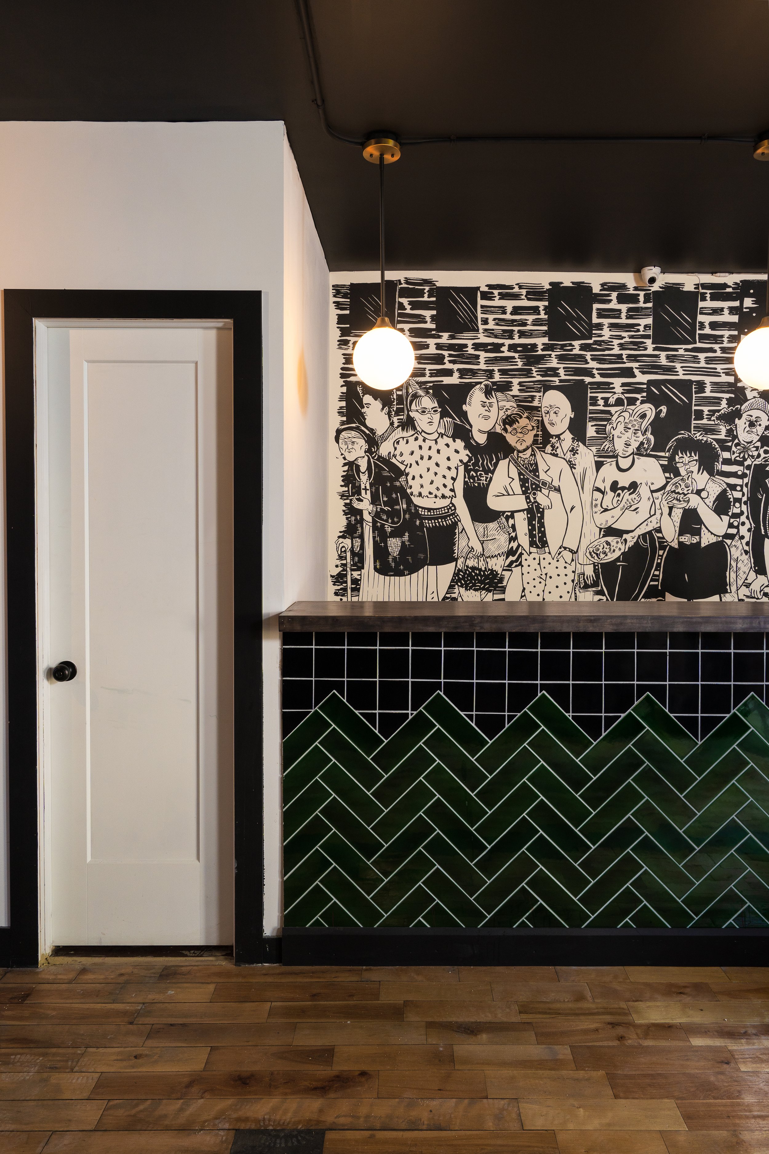 Dark green geometric tile wainscoting beneath a black-and-white illustrated mural in the Turbo Haüs bar.