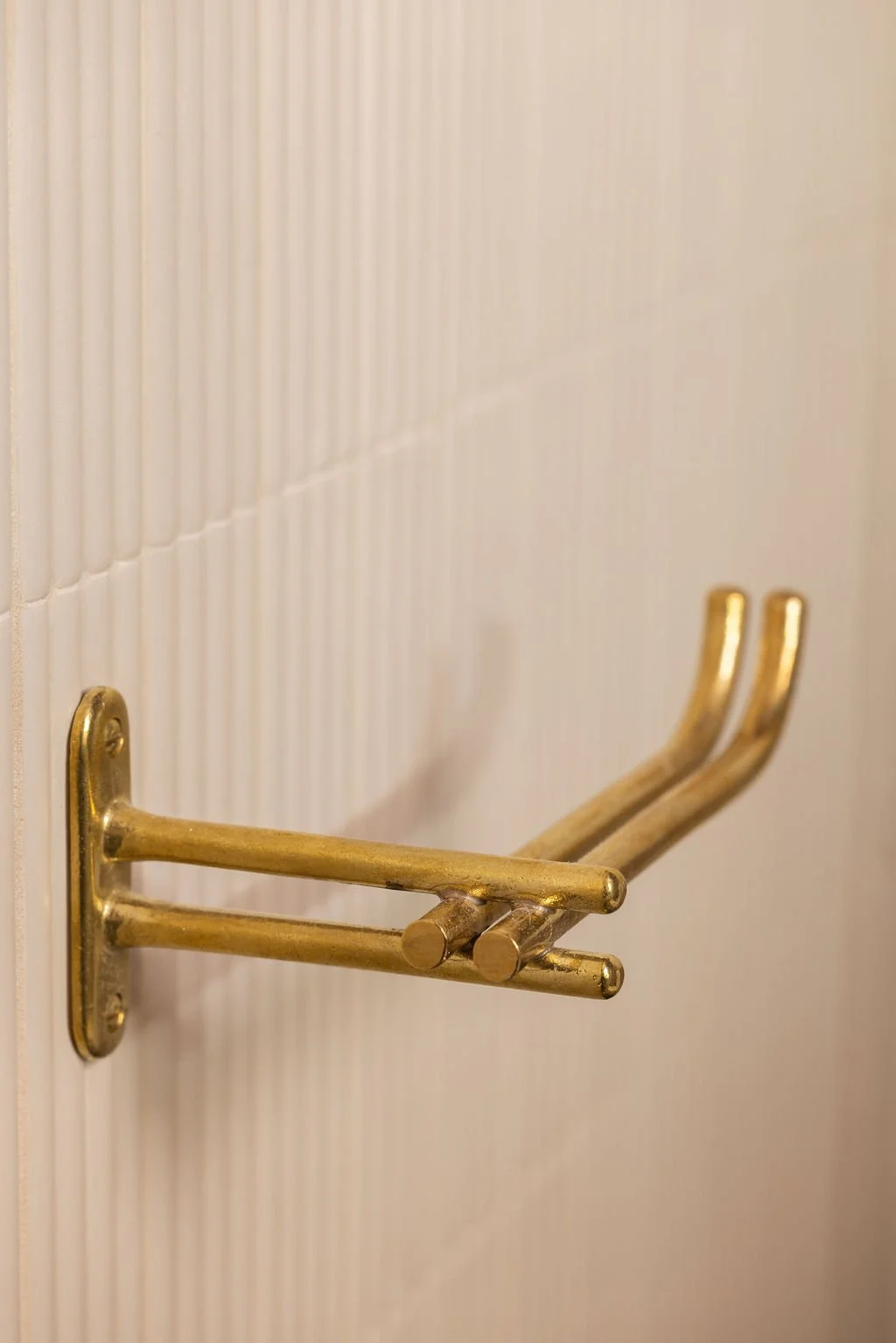 Close-up of a brass wall-mounted accessory hook against pale vertically fluted powder room tile.