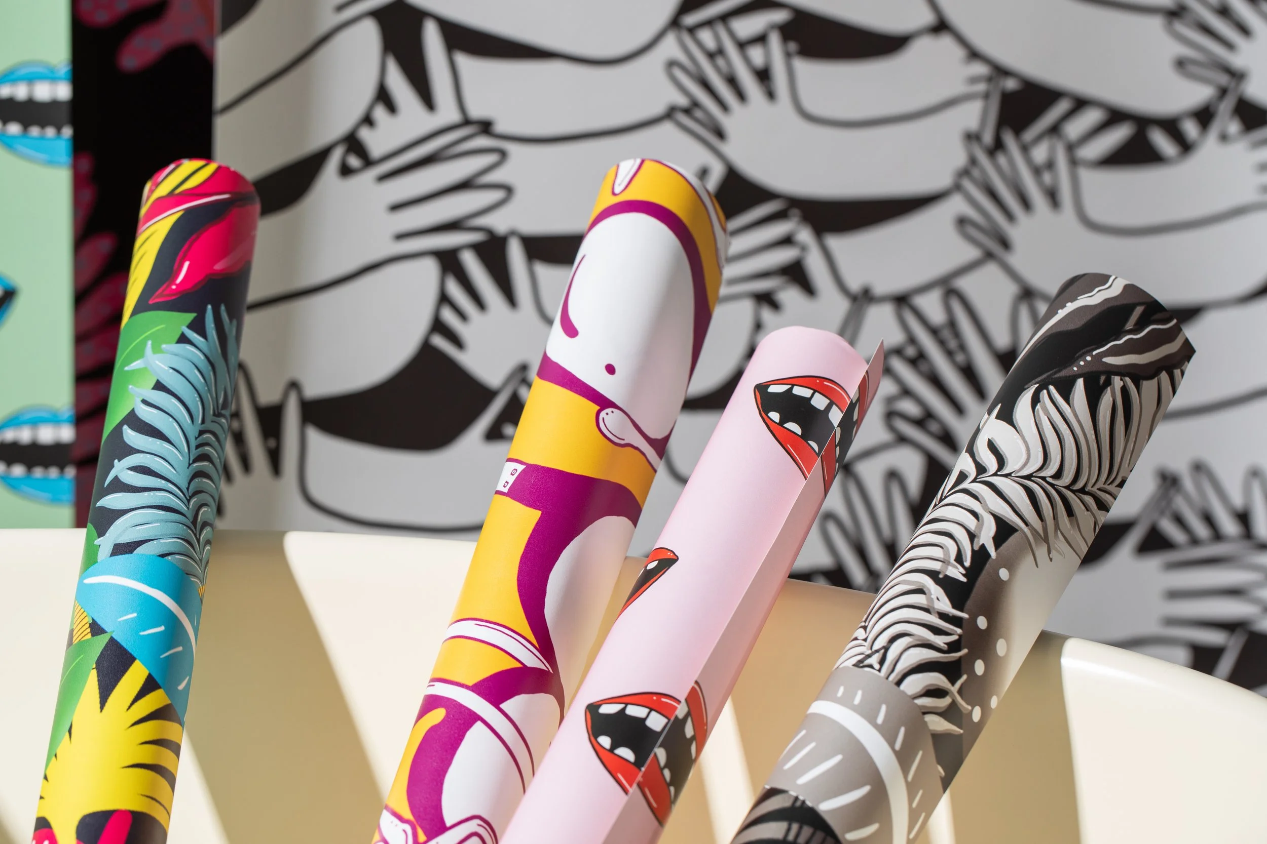 Close-up of colourful illustrated wallpaper rolls against a black-and-white pattern of overlapping hands.