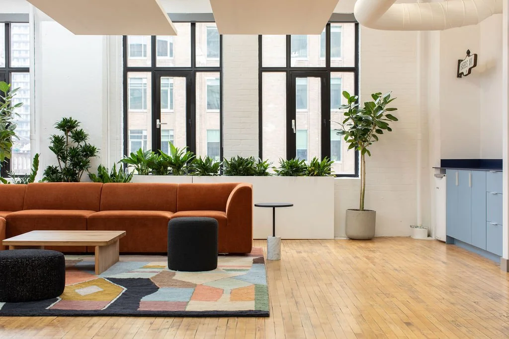 Office lounge at Chef's Plate in Toronto, designed by Flodström Interiors with a rust-coloured sofa, geometric area rug, indoor plants and large industrial windows.