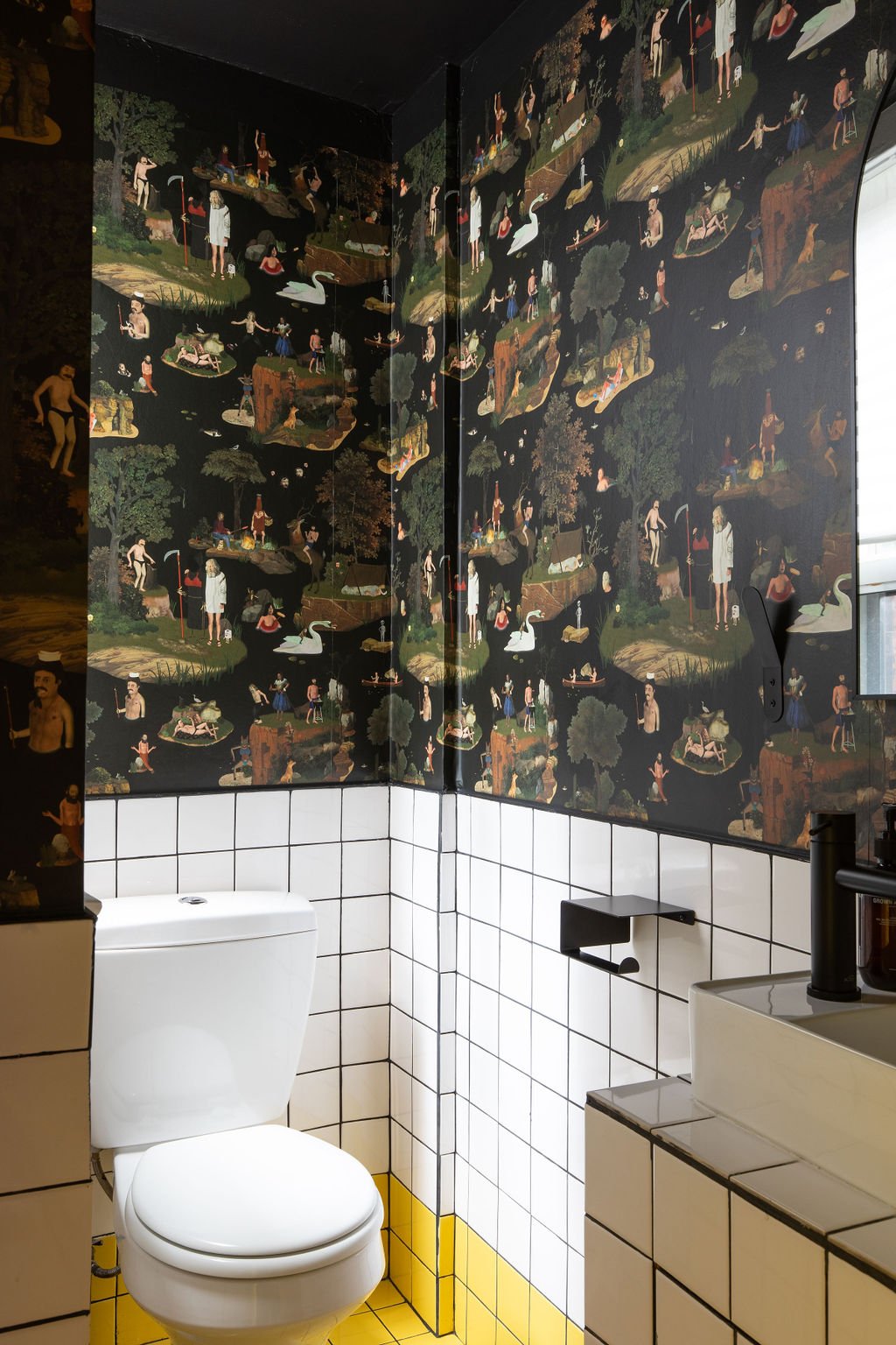 Eclectic studio washroom with dark illustrated wallpaper, white square tiles, black fixtures and a yellow accent.
