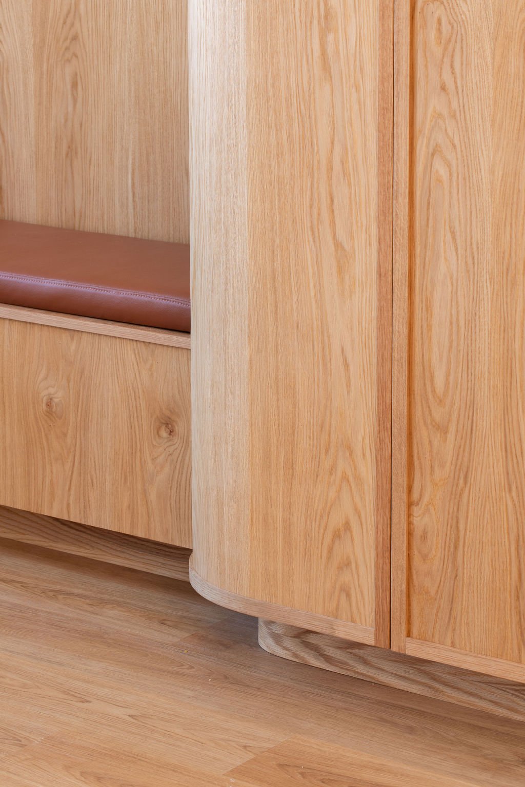 Close-up of custom oak cabinetry showing the curved cabinet base, natural wood grain and adjoining built-in bench with terracotta upholstery.