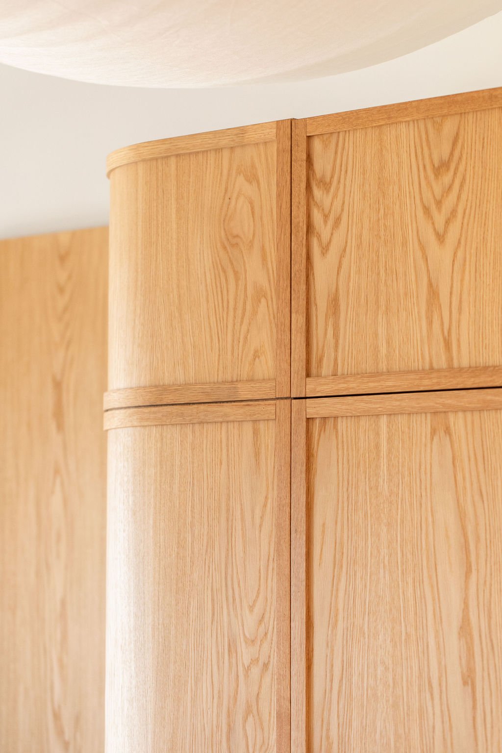 Close-up of rounded oak cabinetry showing the curved corner, continuous wood grain and precisely aligned horizontal and vertical panel divisions.
