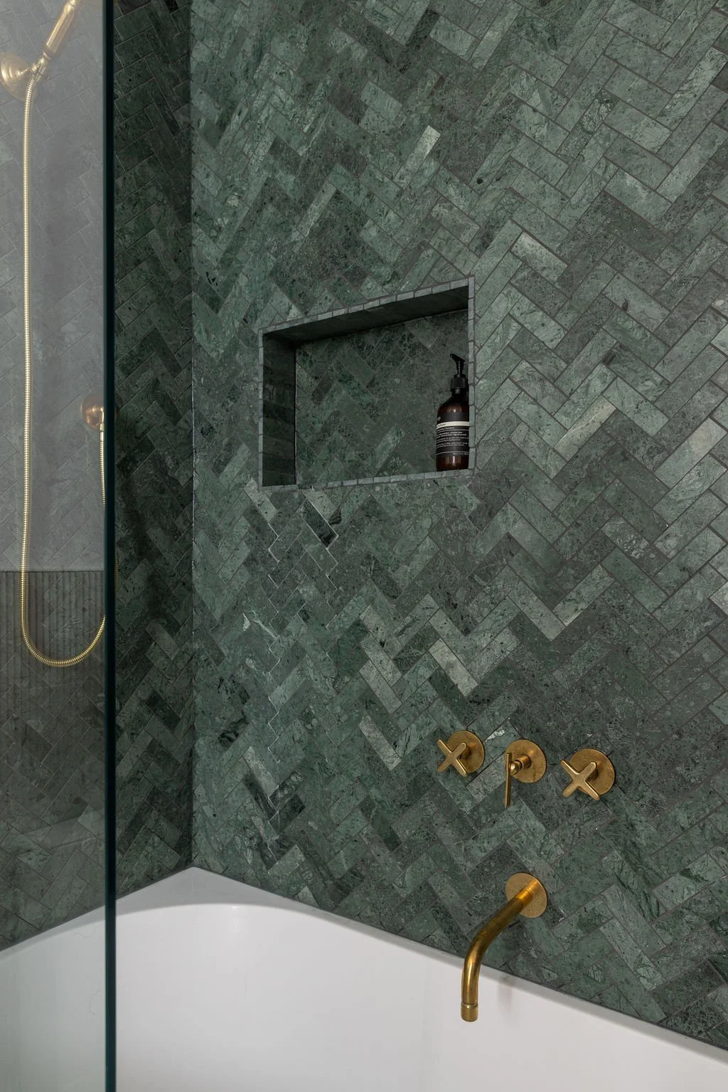 Green herringbone stone shower wall with a recessed storage niche and brass shower fixtures.