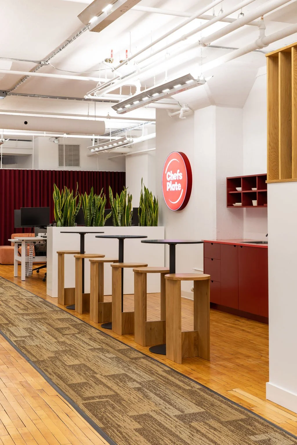 Collaborative workspace at the Chef's Plate Toronto office, designed by Flodström Interiors with standing-height tables, custom wood stools, red cabinetry and integrated greenery.