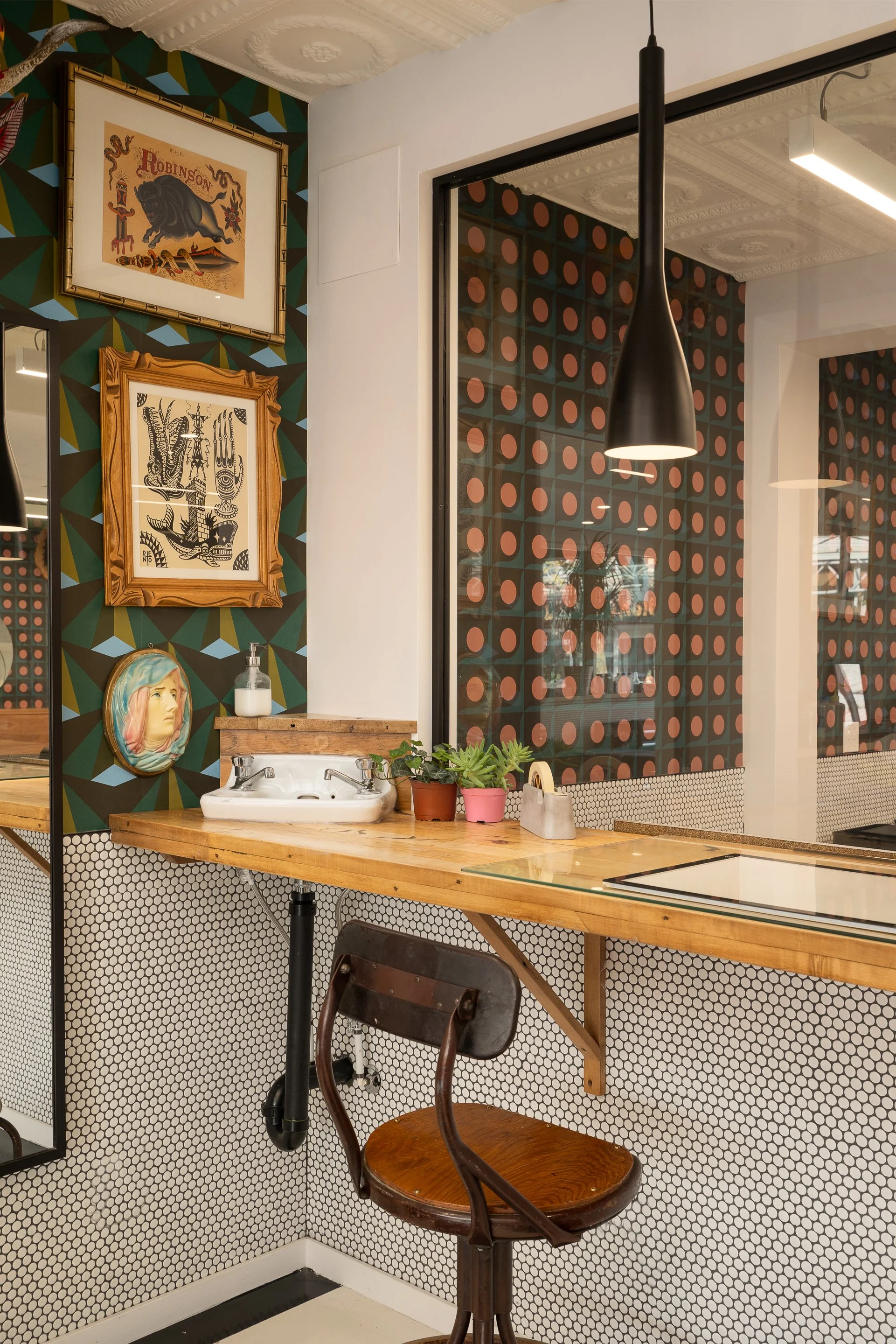 Glass partition and display wall covered in framed tattoo flash artwork, separating the tattoo studio from the salon.