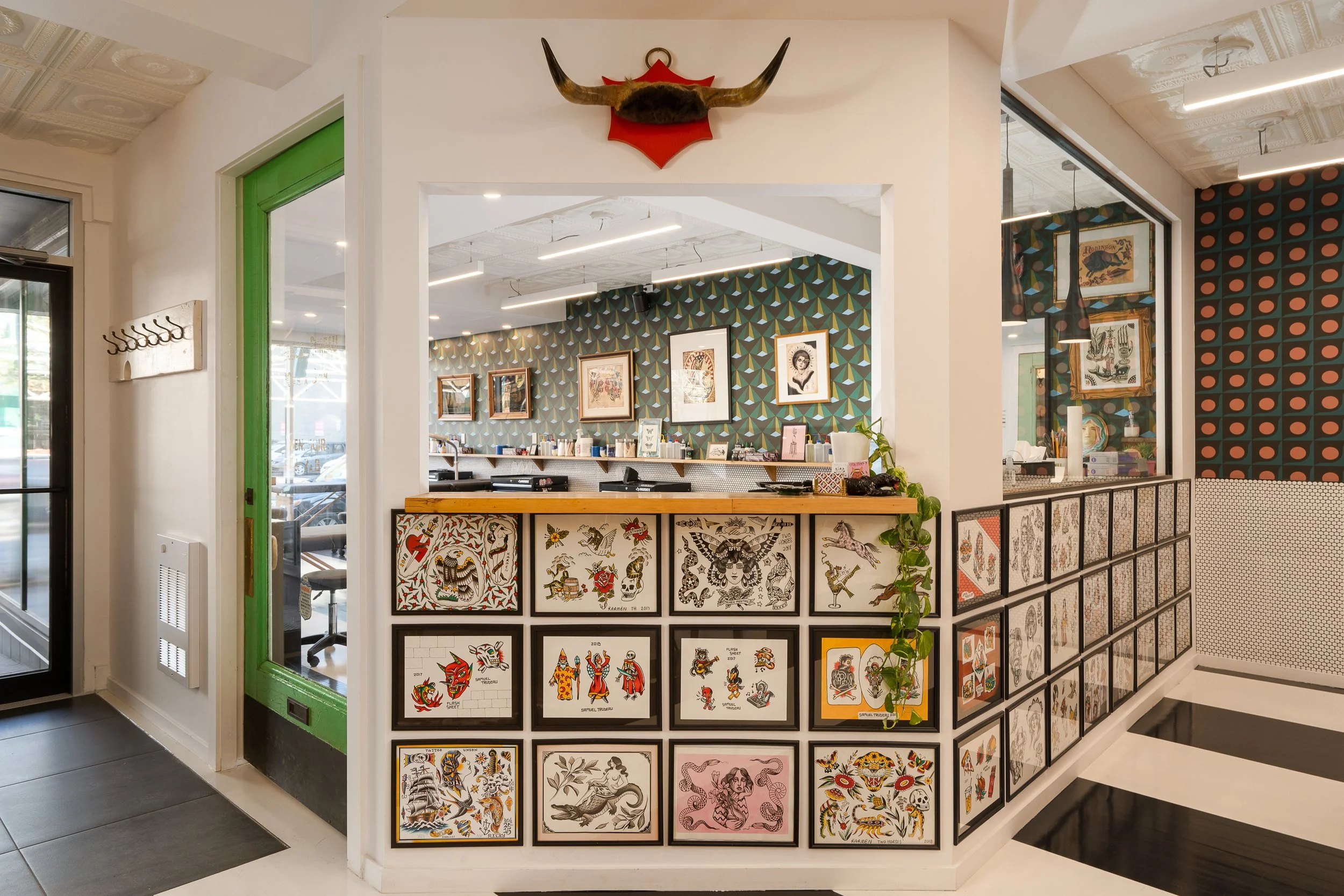 Entrance to the Two Horses tattoo studio with a green door, mounted horns and a display of framed tattoo flash artwork.