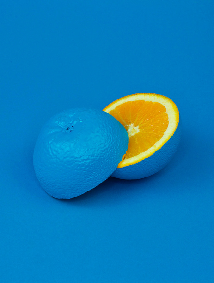 Blue-painted orange with a bright orange slice against a blue background, illustrating the contrasting colour inspiration for the CLA/ACL identity.