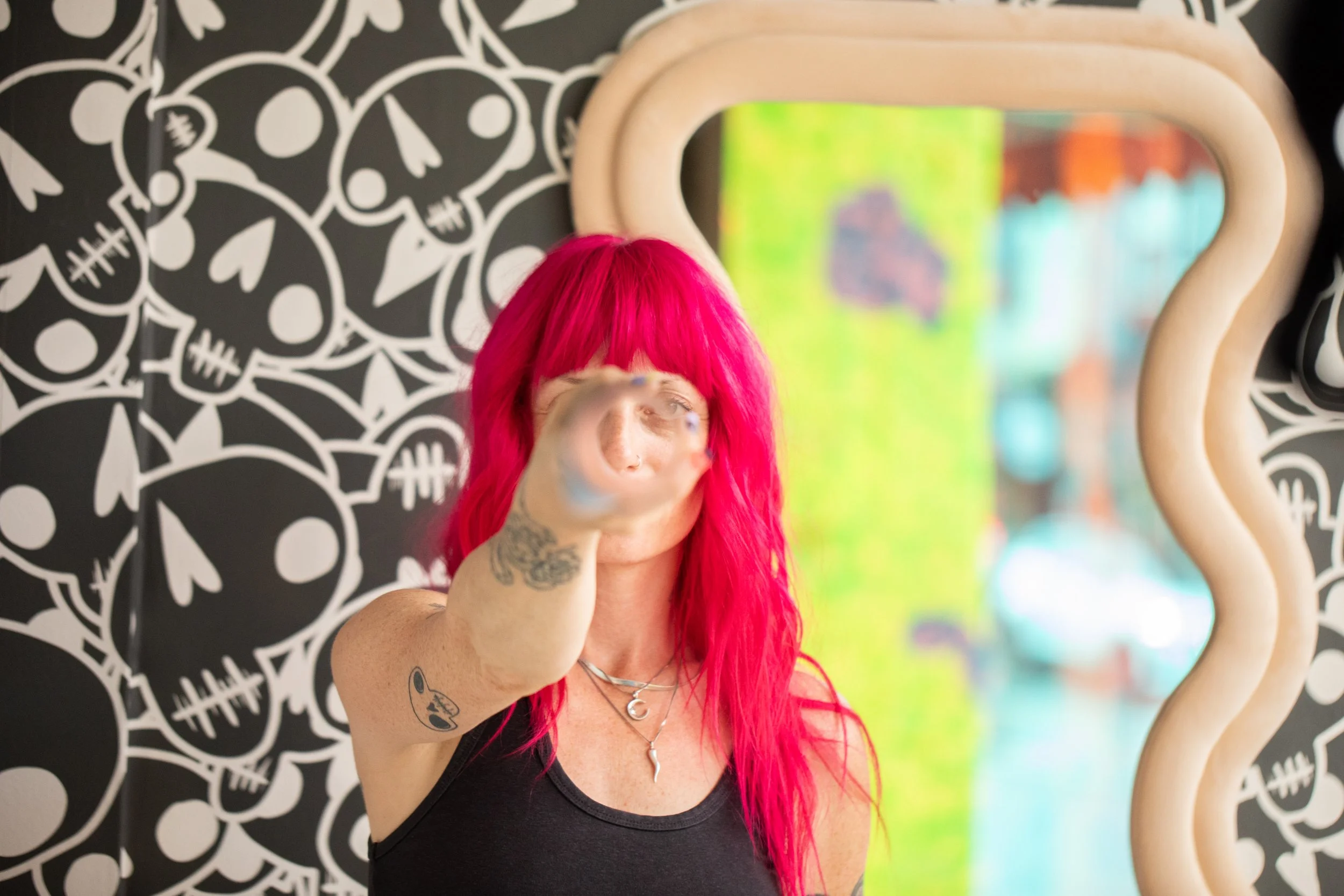 Portrait of a pink-haired designer in front of black-and-white illustrated wallpaper and an organically shaped mirror.
