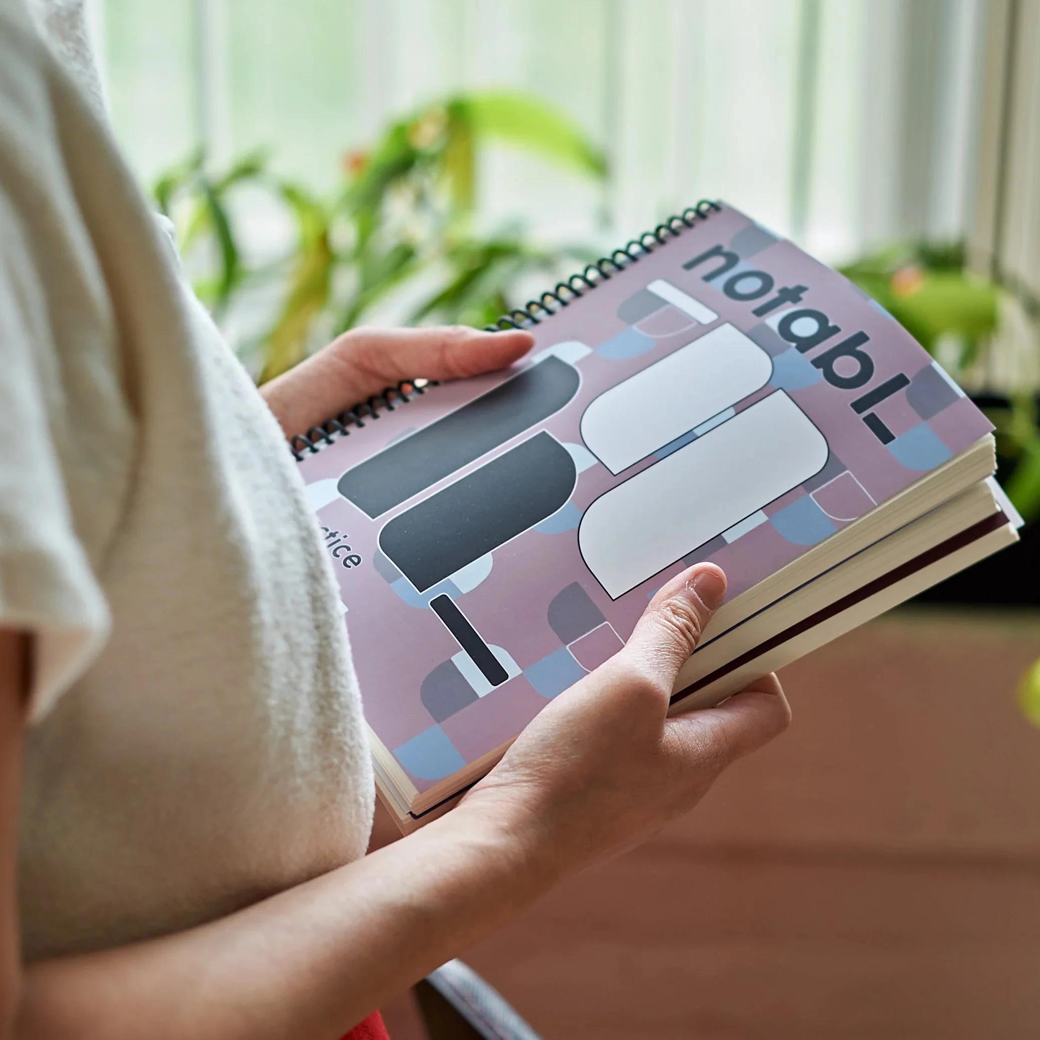Person holding the spiral-bound Notabl. practice journal for musicians, featuring a mauve cover with oversized geometric lettering and an abstract pattern.