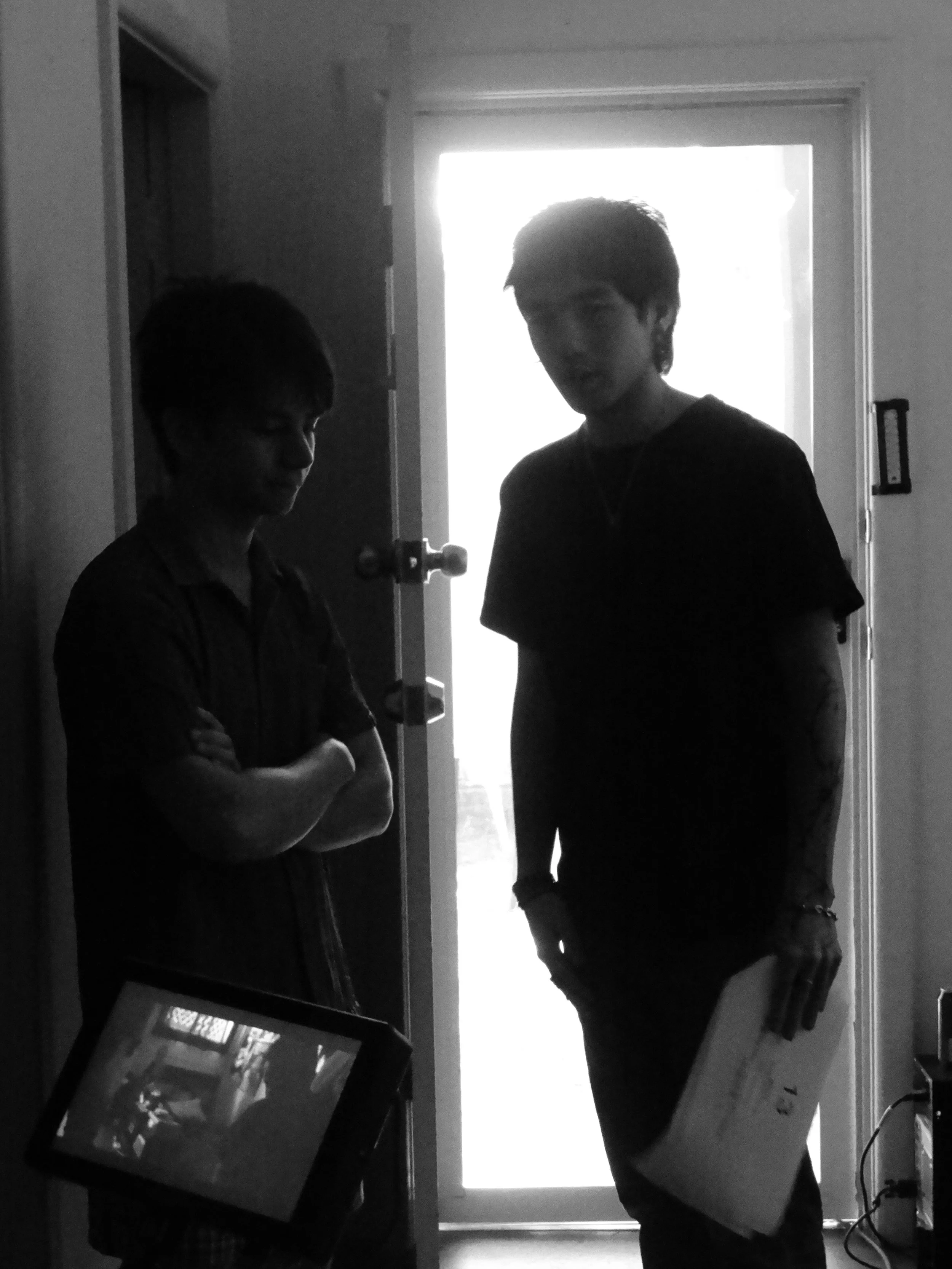 Black-and-white photo of two people standing in a doorway, with one holding a tablet.