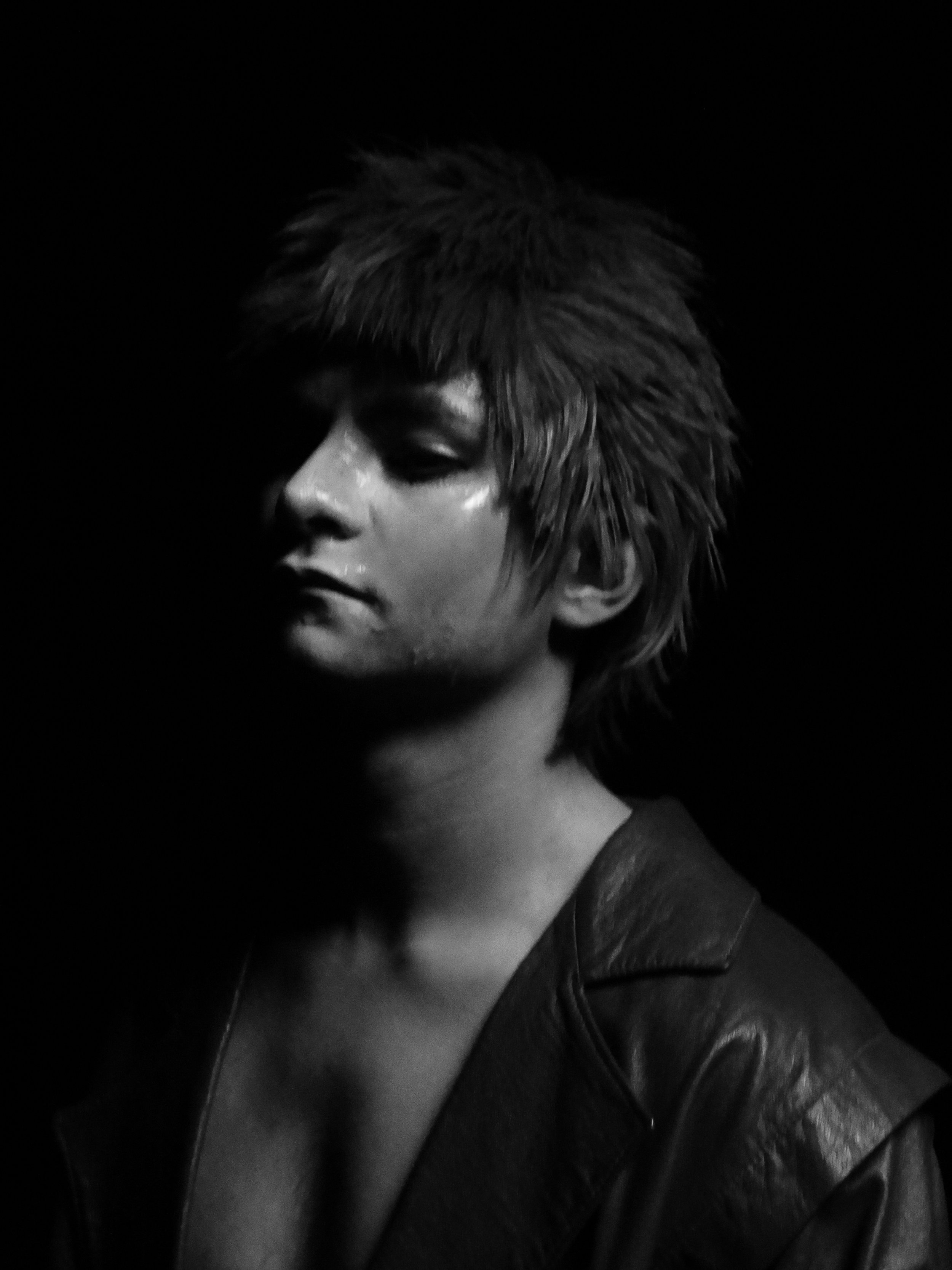 Black-and-white close-up portrait of a person with shaggy hair and closed eyes against a dark background