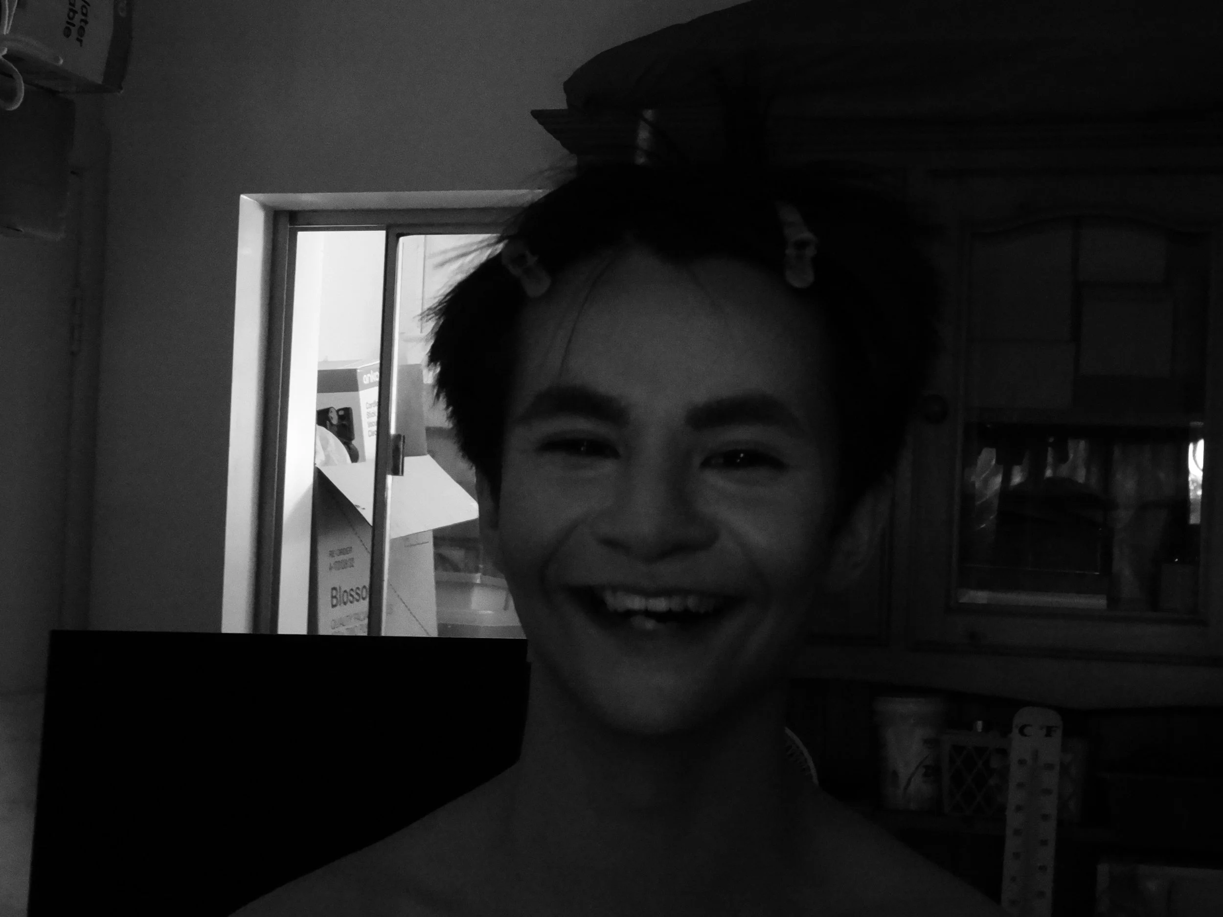 Black-and-white close-up selfie of a smiling person wearing a baseball cap indoors