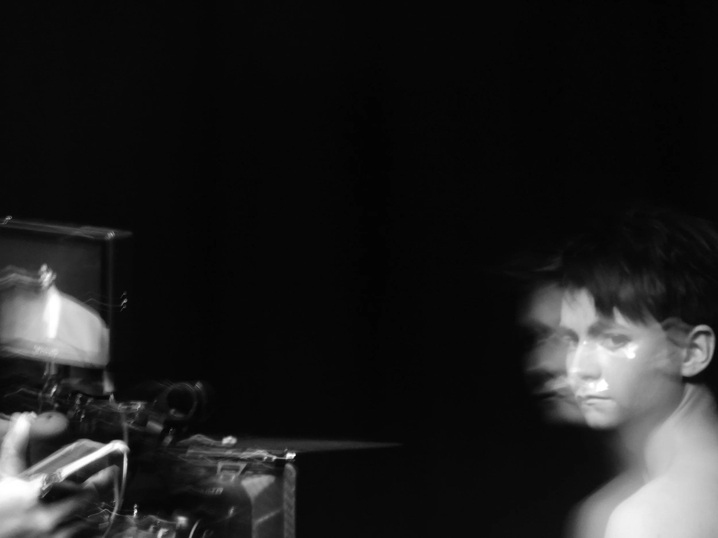 Black-and-white photo of a drummer playing an electronic drum kit beside a smiling man in a dark setting.