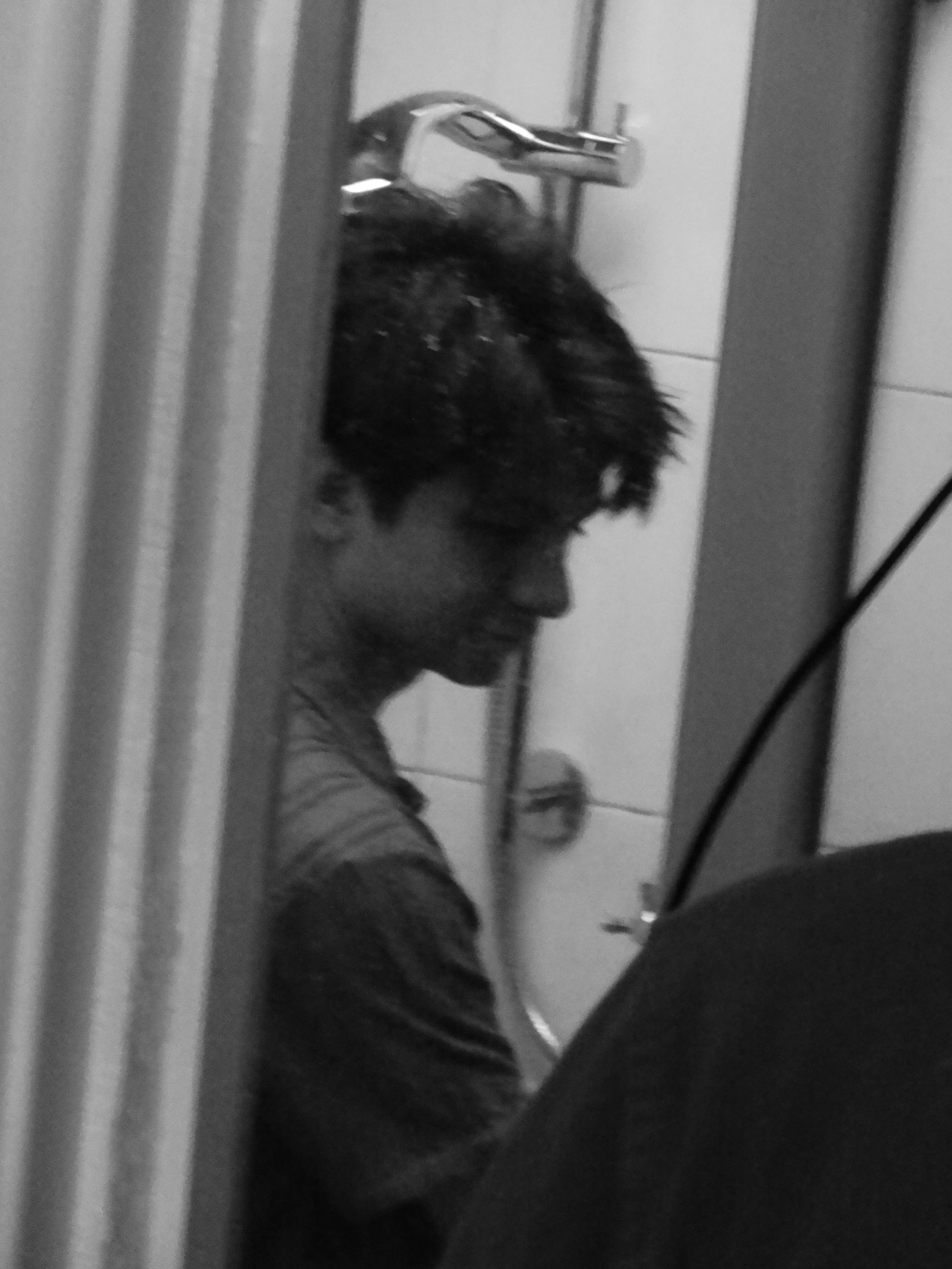 Black-and-white side profile of a bearded man wearing glasses and a dark sweater in front of a tiled wall