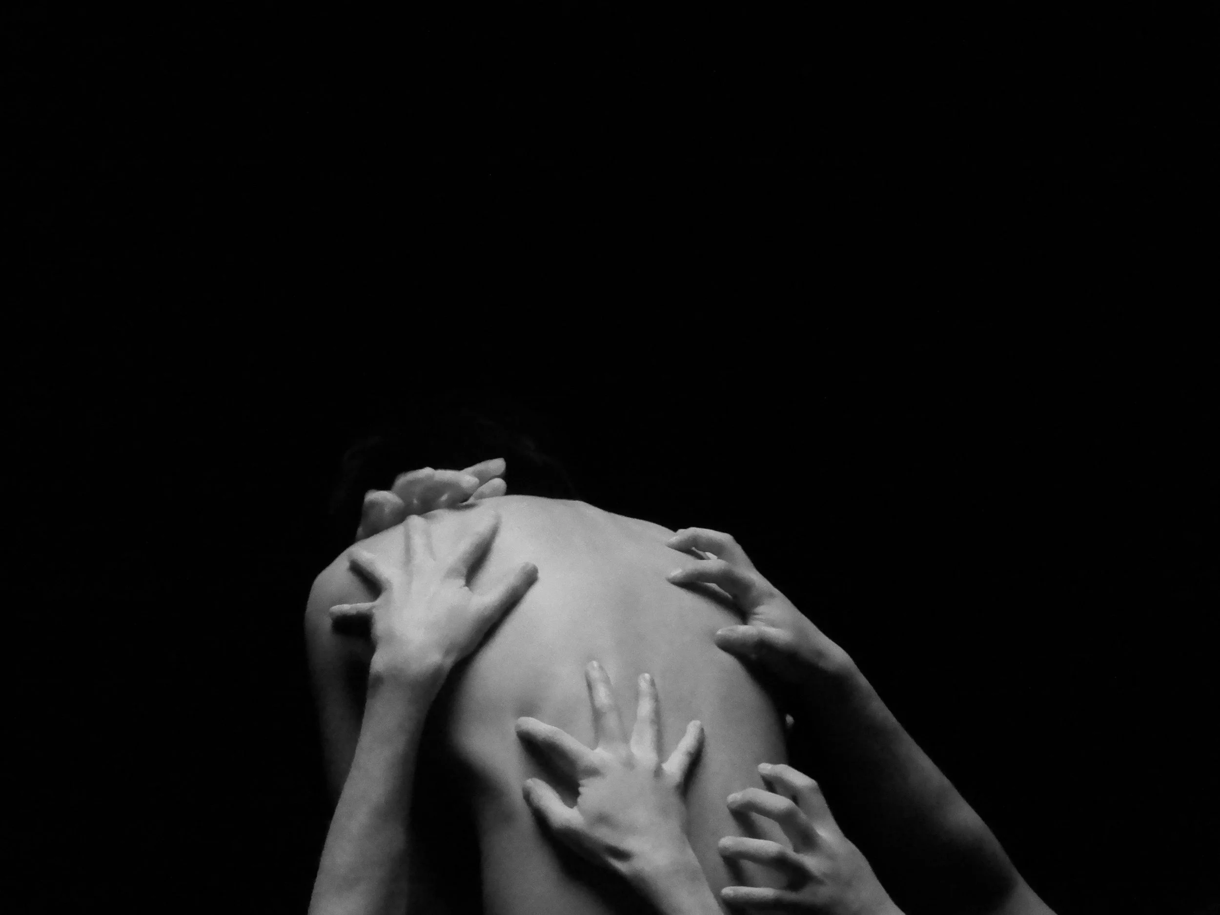Black-and-white image of several hands touching a person's bare back against a dark background